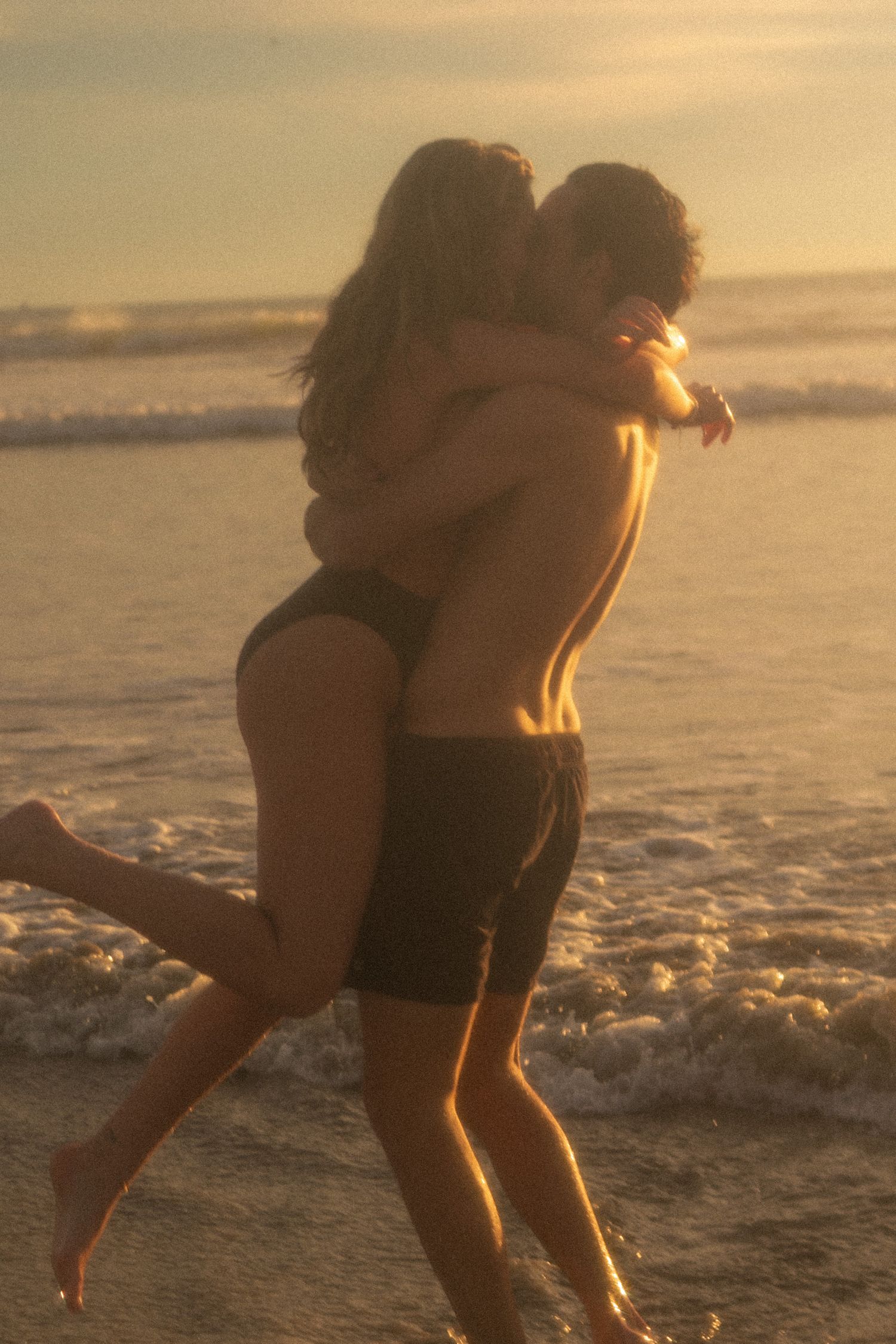 A romantic silhouette of a couple embracing on the beach at sunset with gentle waves rolling in the background.