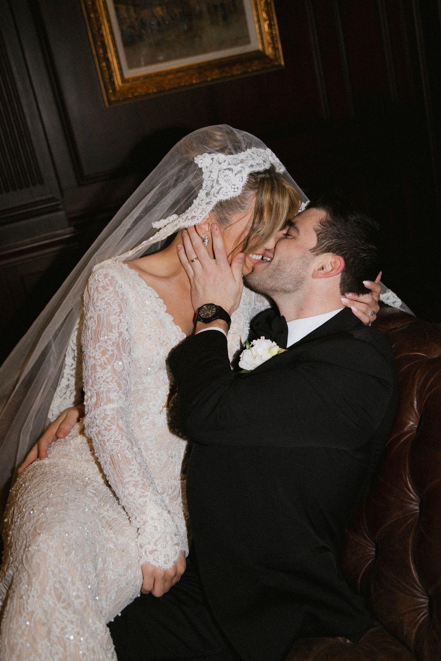 Candid wedding moment captured on leather couch with intimate embrace.