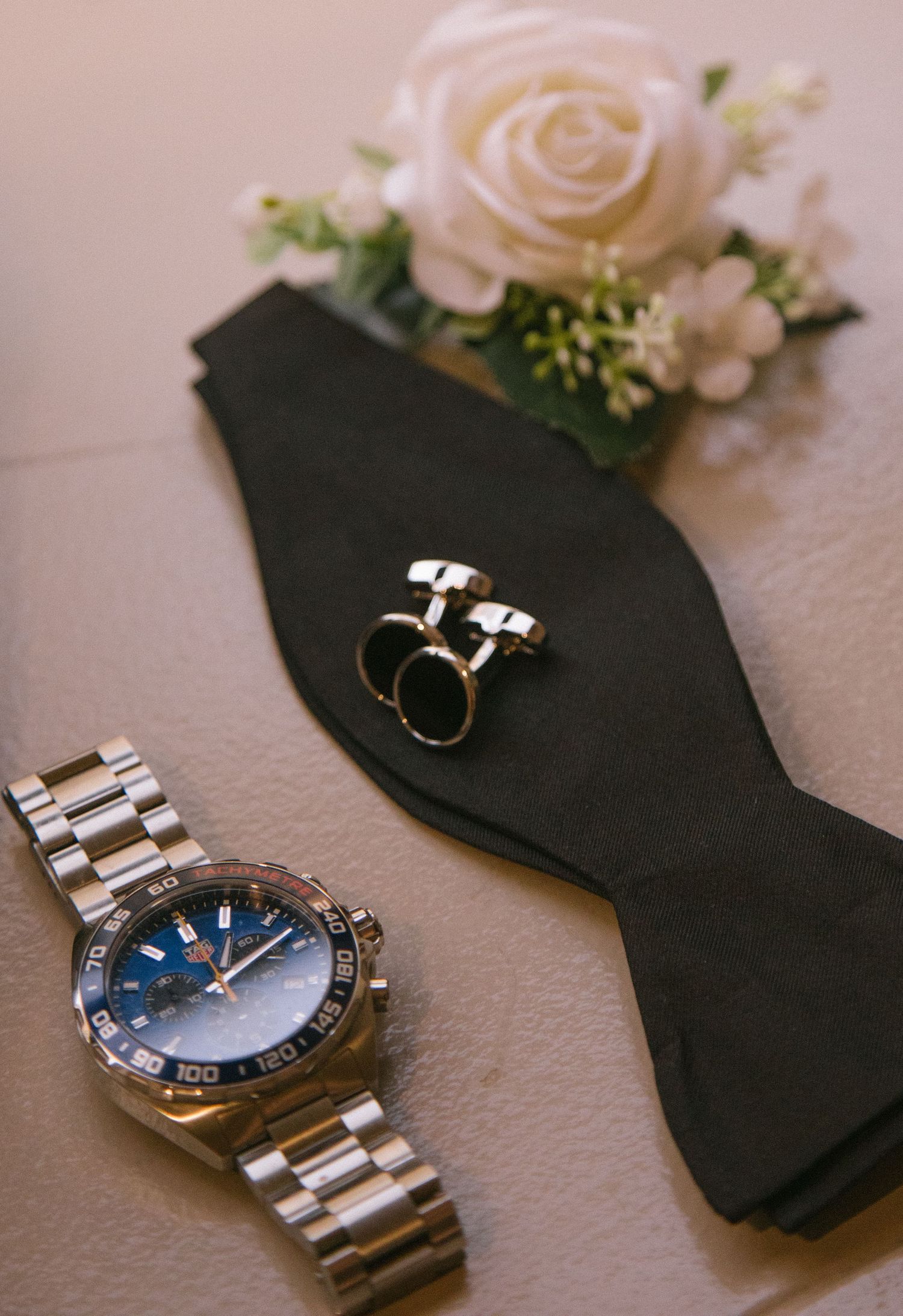 Elegant silver wristwatch with blue dial and metal bracelet displayed alongside white roses and black fabric on light surface.