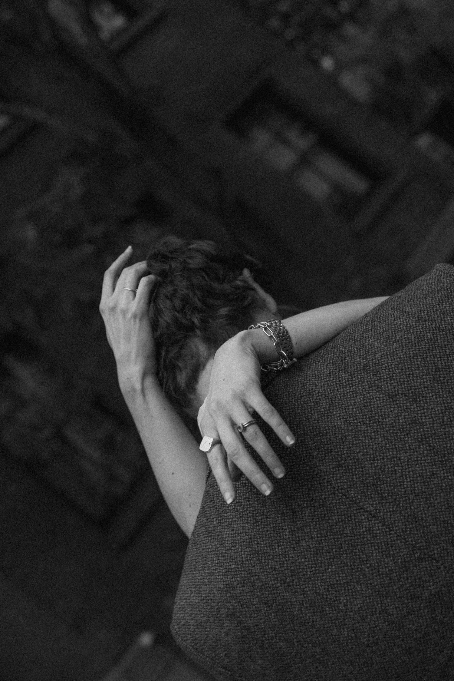 Black and white close-up of hands with rings resting on a dark surface, showing intimate body language.