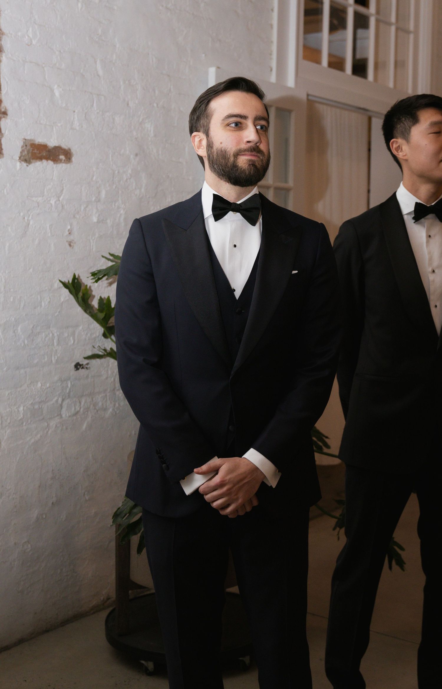 Groomsmen in formal black tuxedos and bow ties stand waiting during a wedding ceremony.