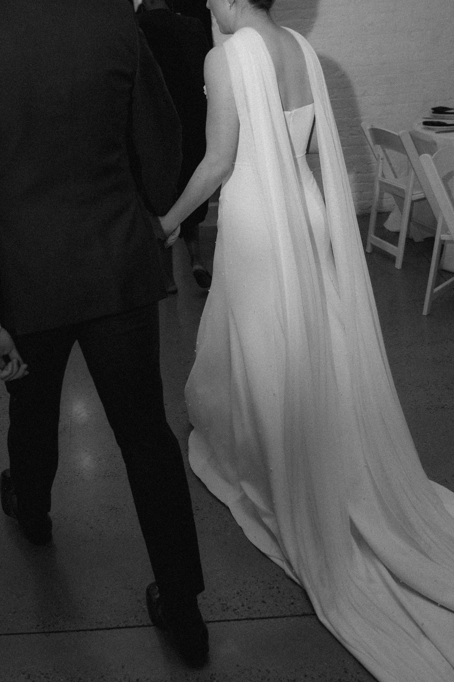Black and white photo showing the dramatic train of a wedding dress as couple walks.