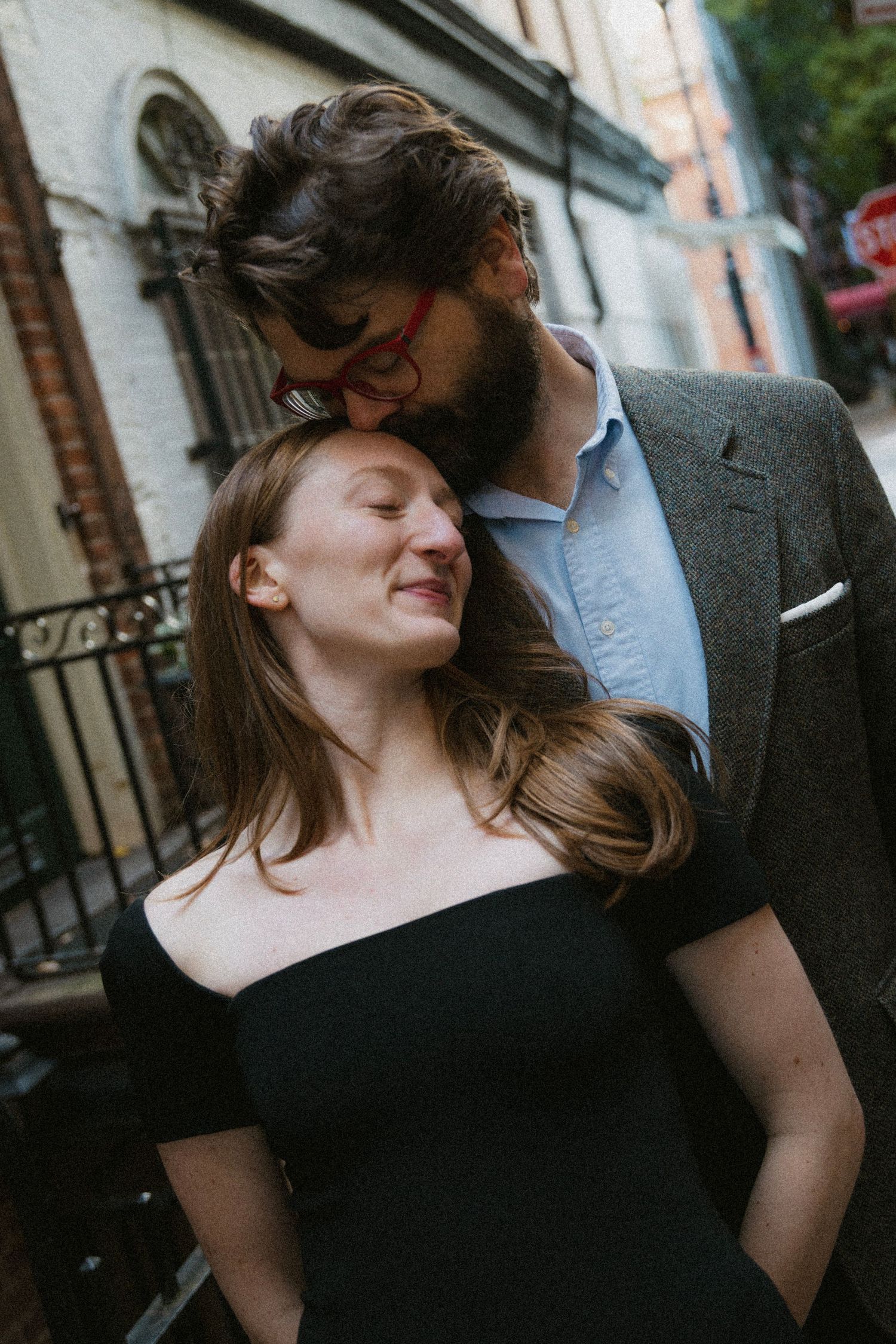 A couple shares an intimate moment together on a city street, her hair blowing in the wind as she leans back.