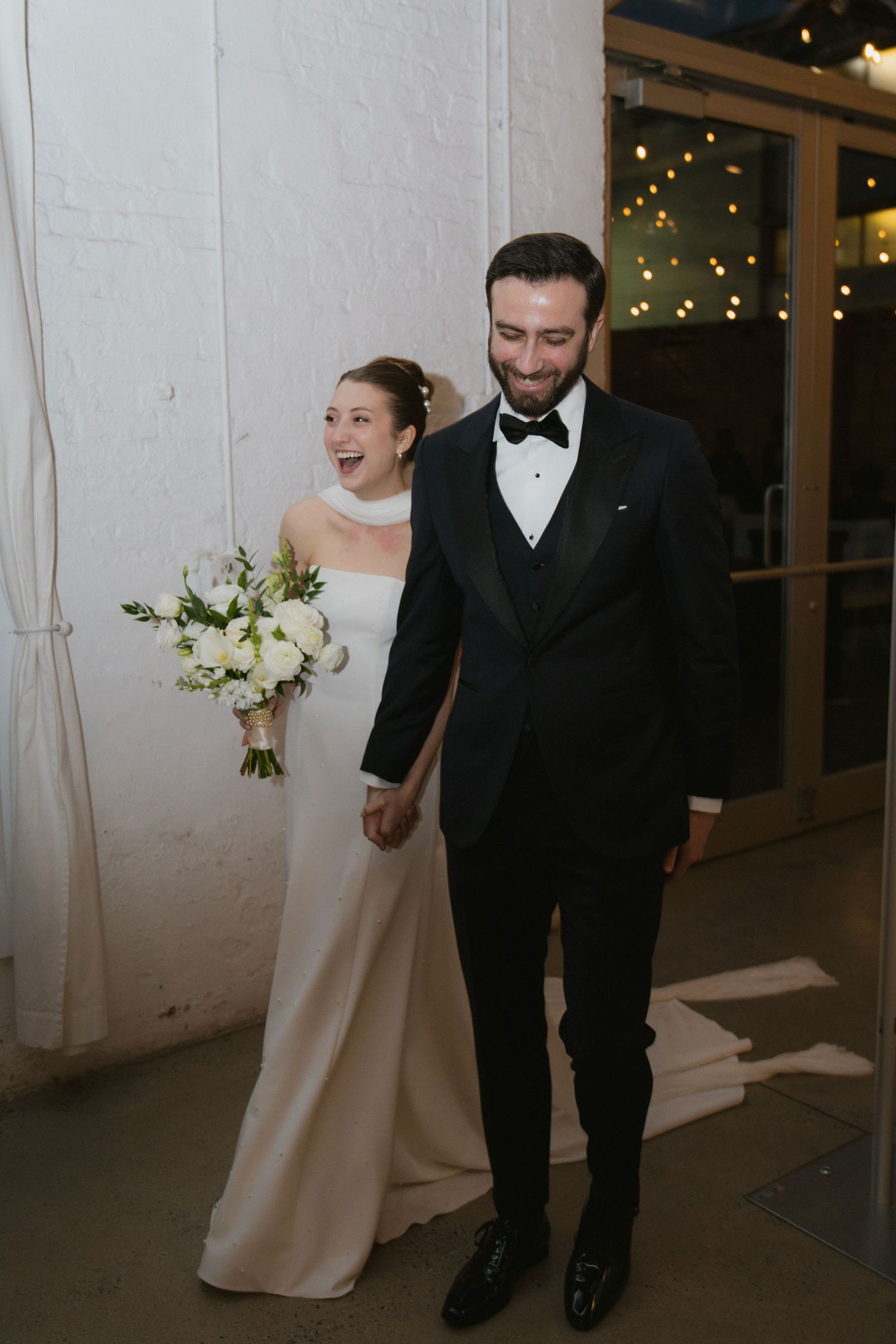 A happy couple walking together after their wedding ceremony with the bride holding a white floral bouquet.