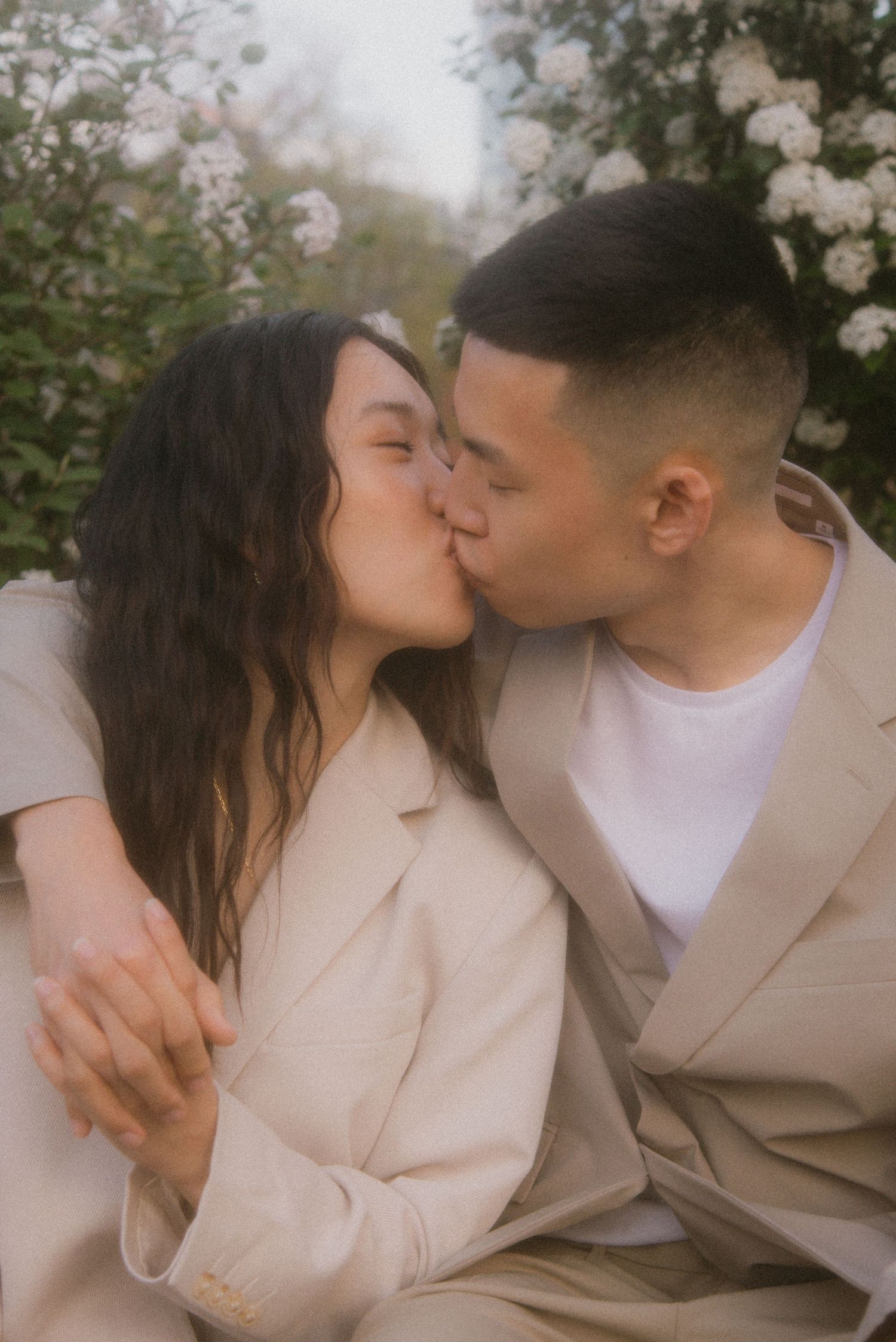 A romantic moment captured between two people in beige outfits with cherry blossoms blooming in the background.