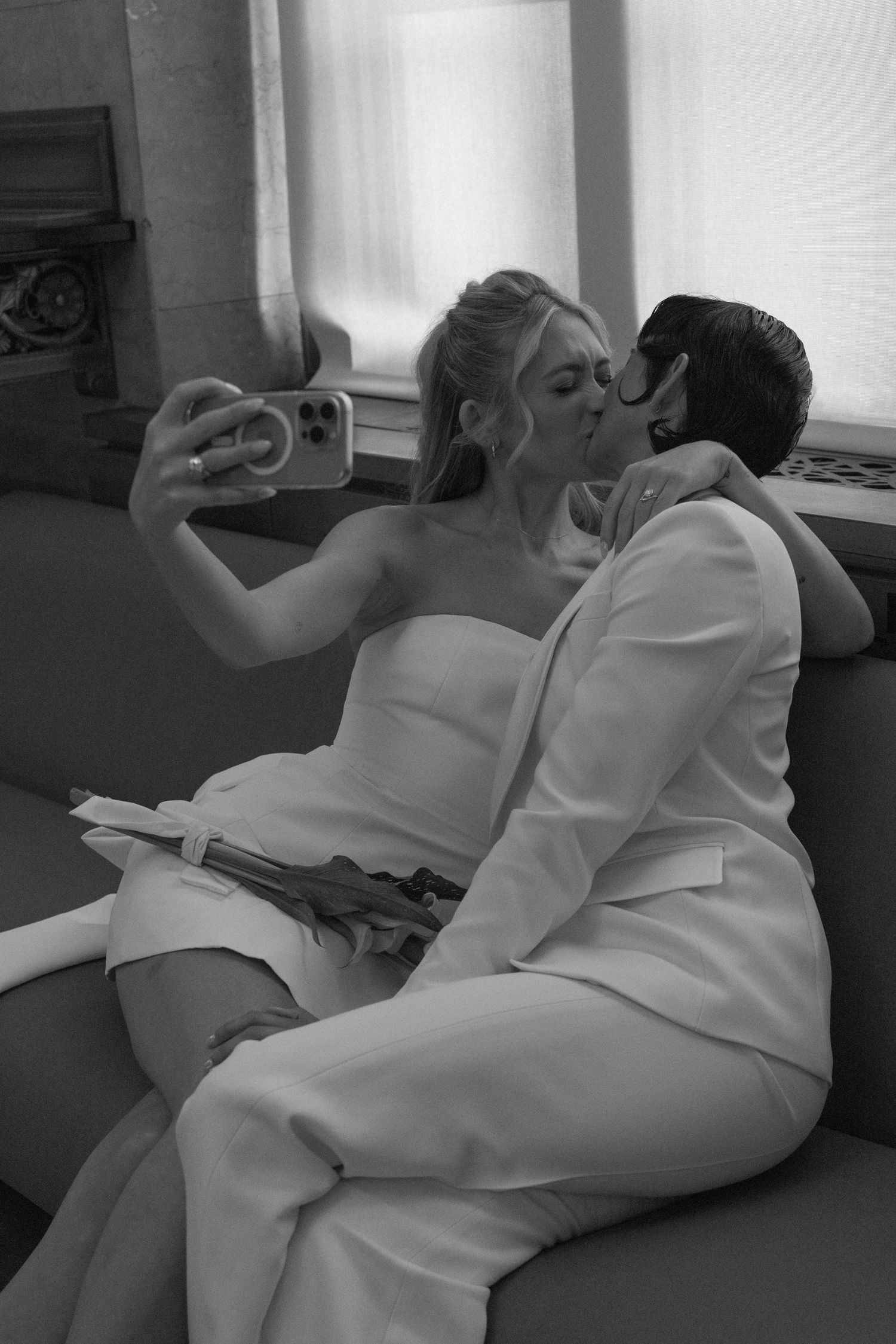 A couple in wedding attire takes a selfie together while sharing an intimate moment.