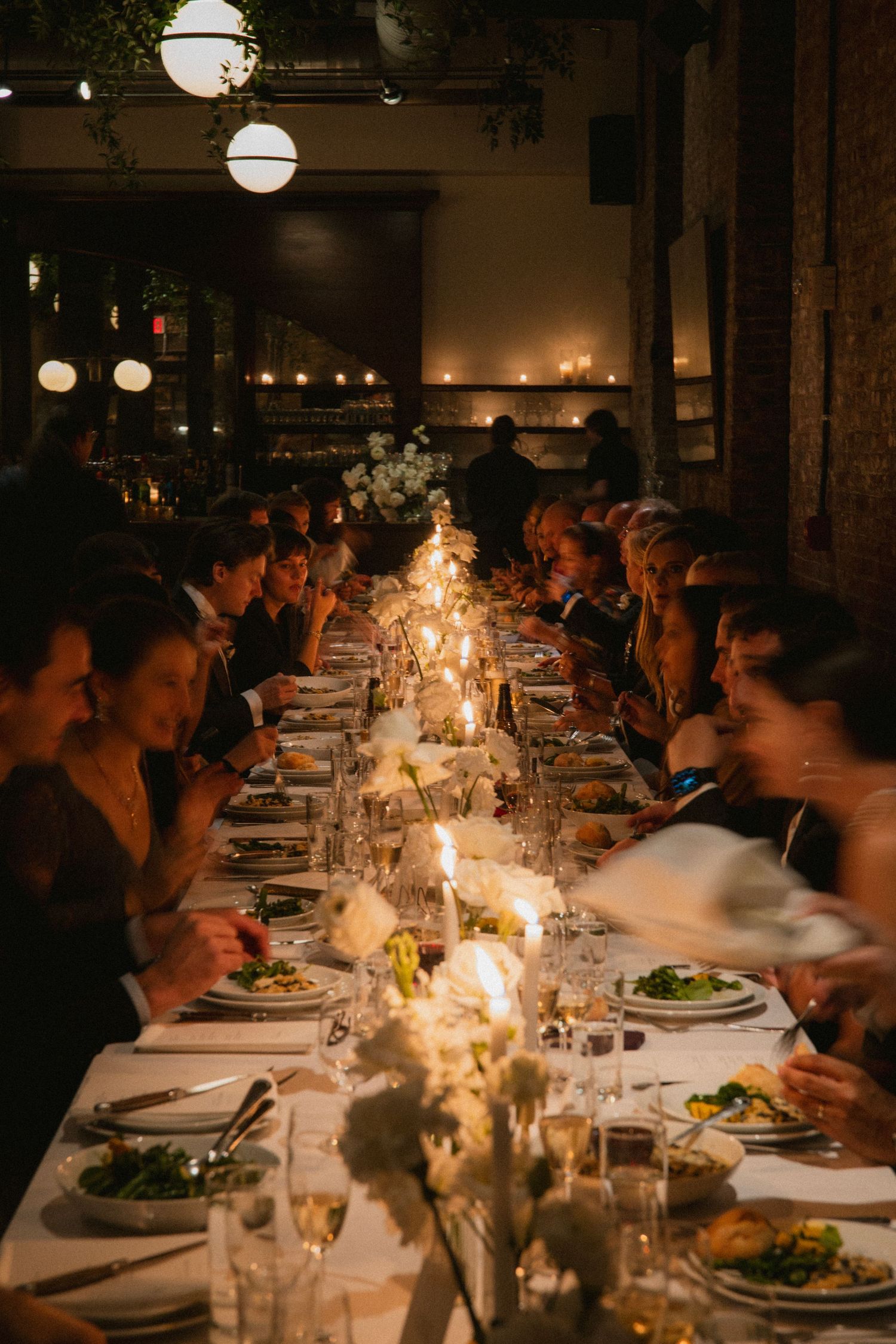 A candlelit dinner table set for a large group with glowing spherical lights above in a romantic restaurant setting.