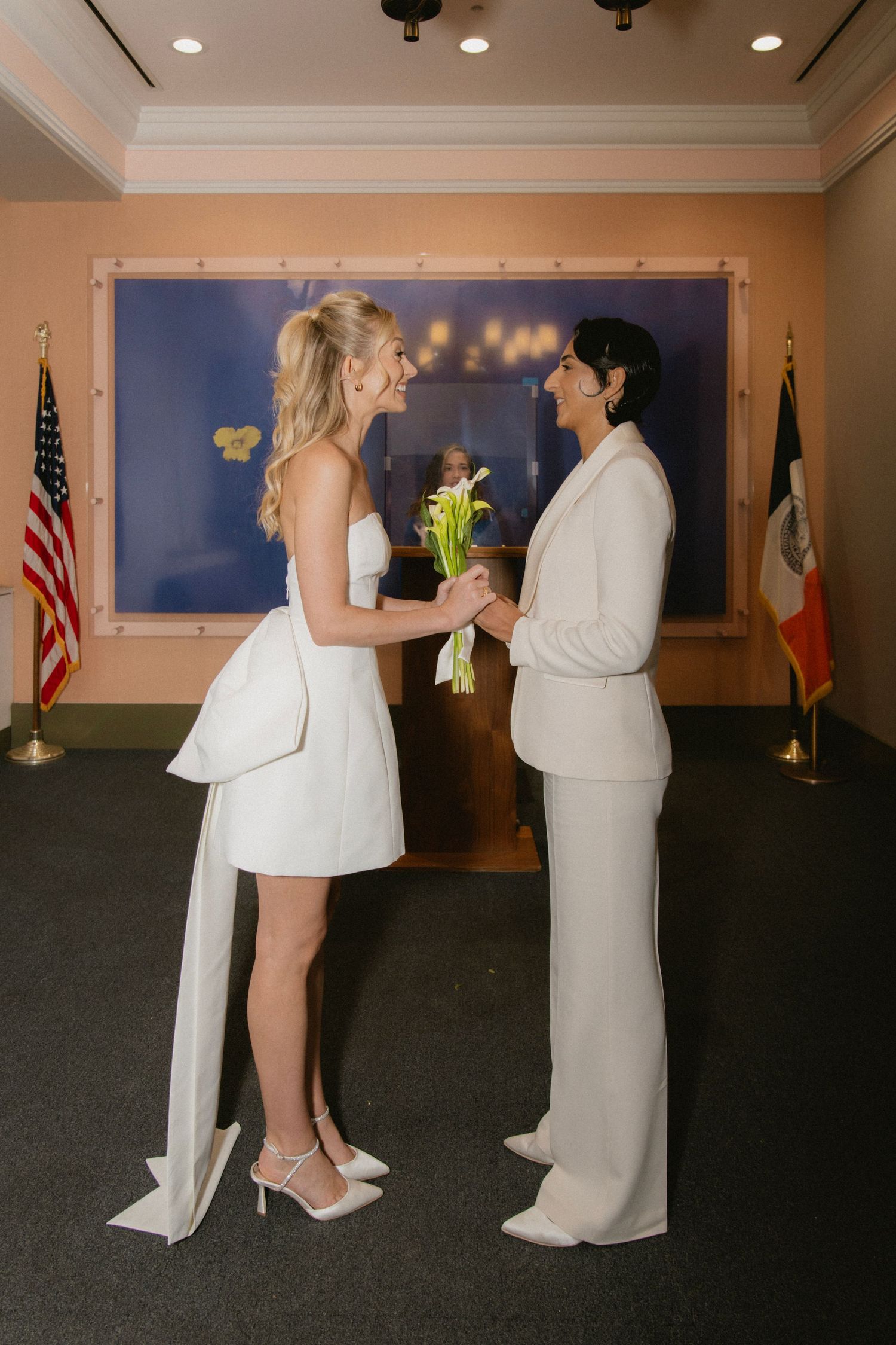 A couple in white attire shares intimate moments during a wedding ceremony in an elegant indoor venue.