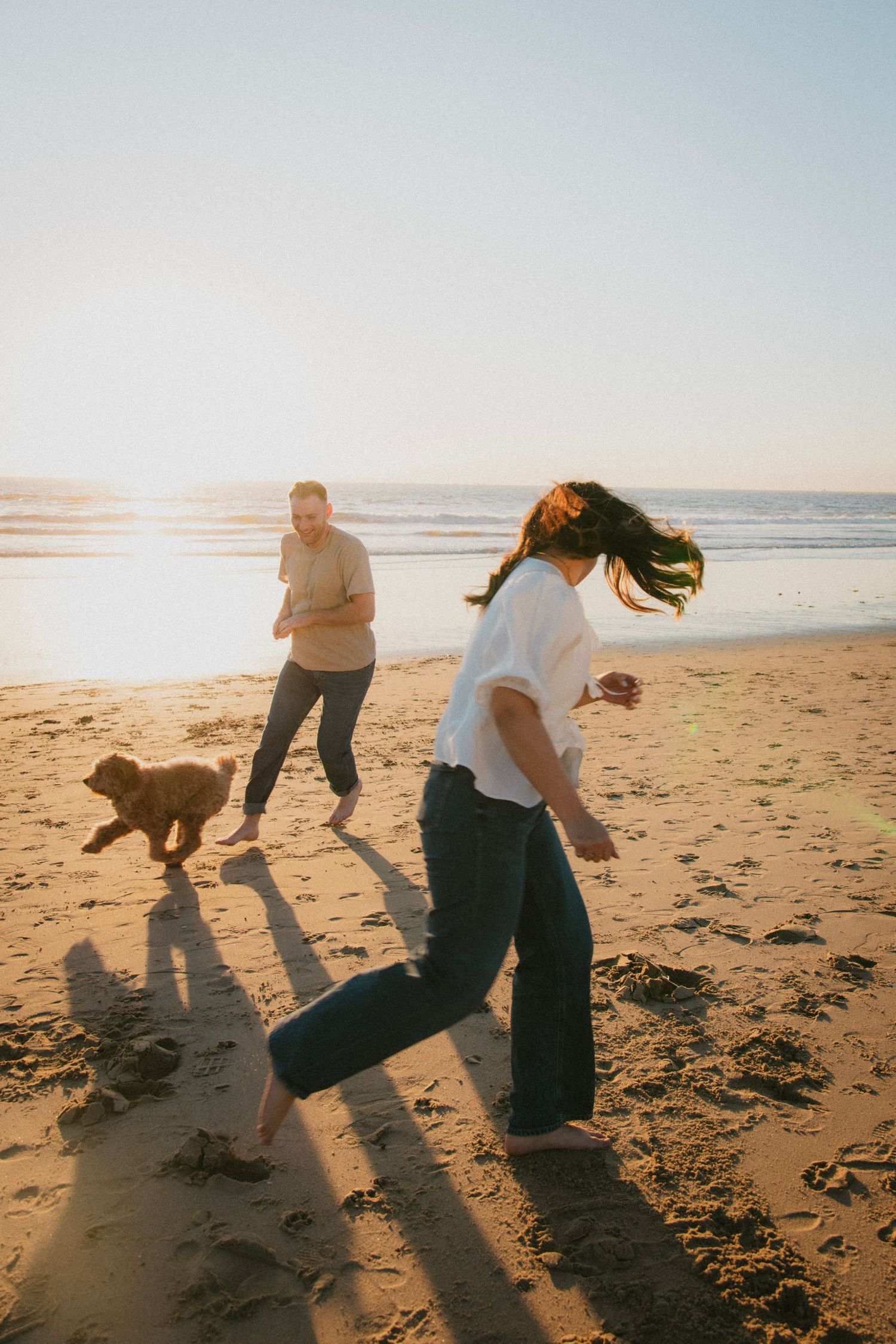 People playing and running on beach at sunset casting long shadows in sand.