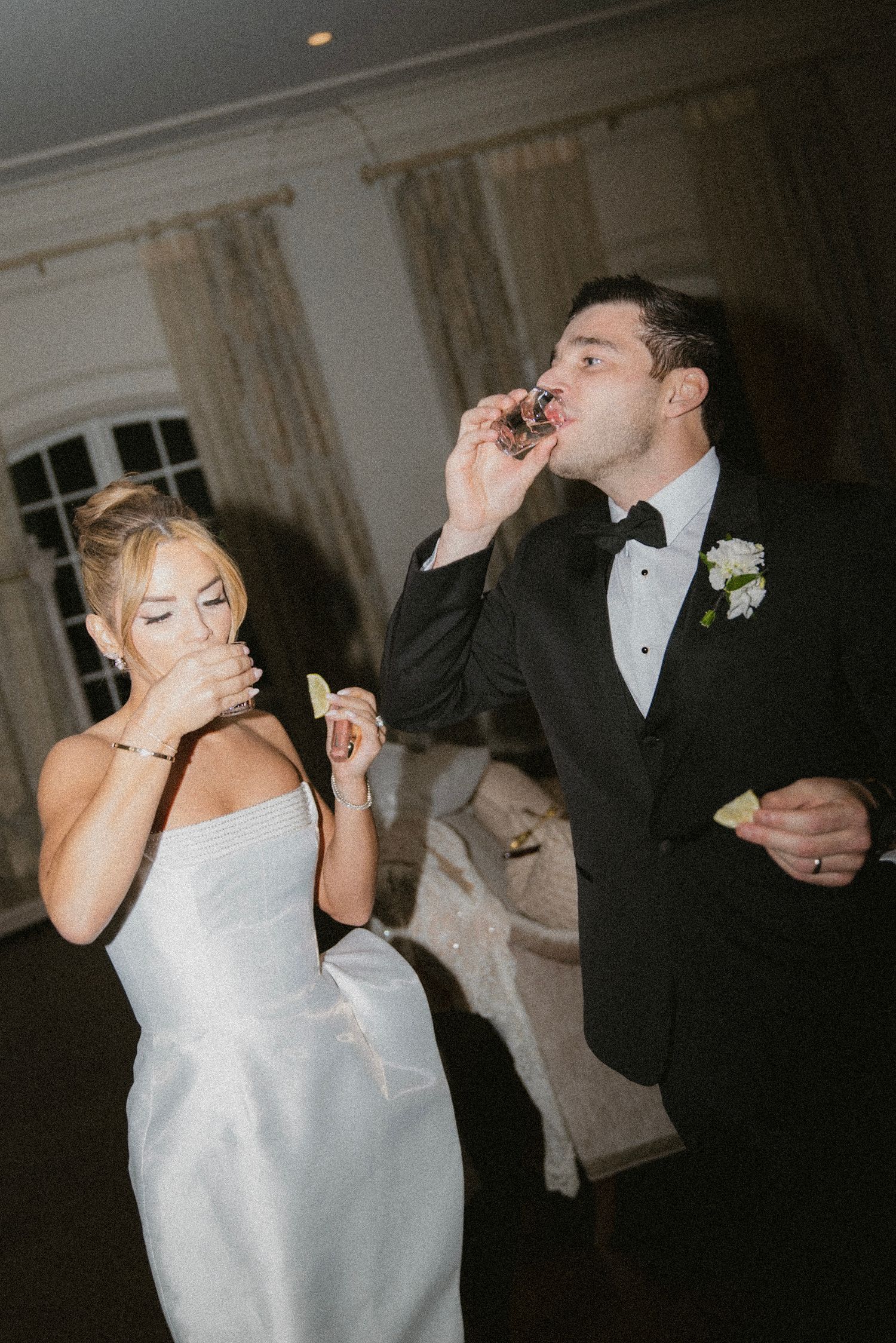 Newlyweds in formal attire sharing a playful moment at their wedding reception.
