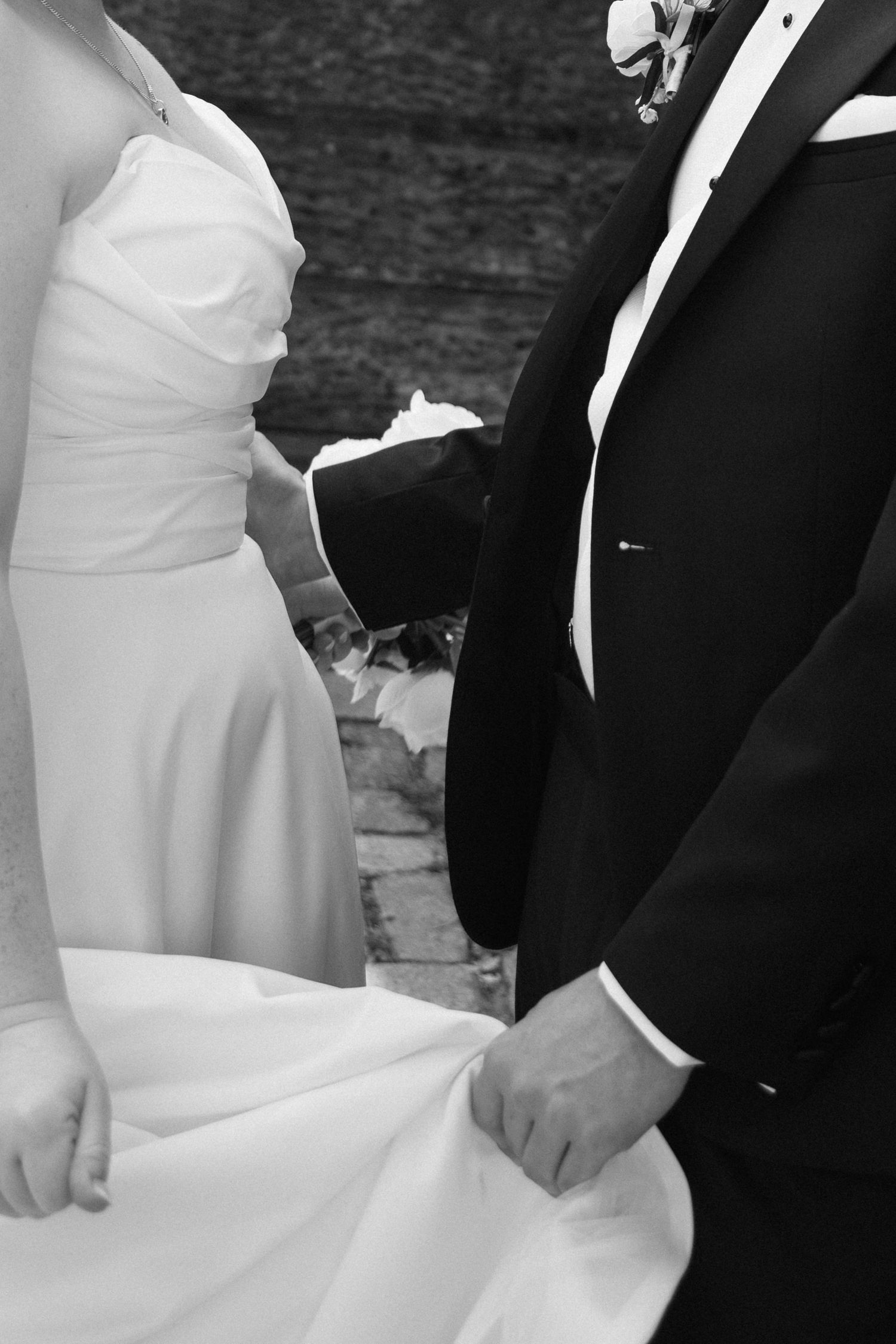 Close-up black and white photograph showing a bride and groom holding hands during a traditional wedding ceremony.