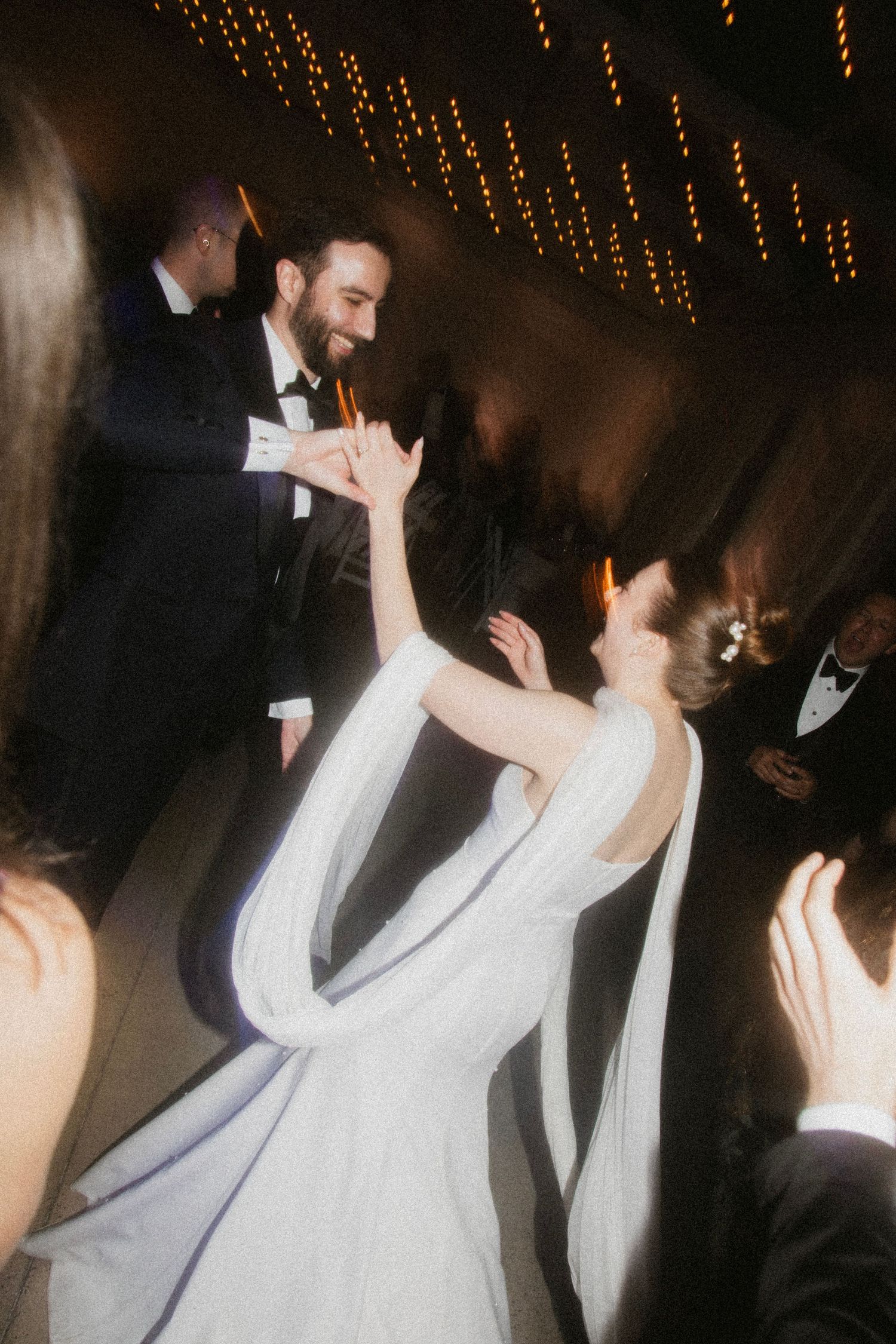 A couple dances together under twinkling lights at their wedding reception.
