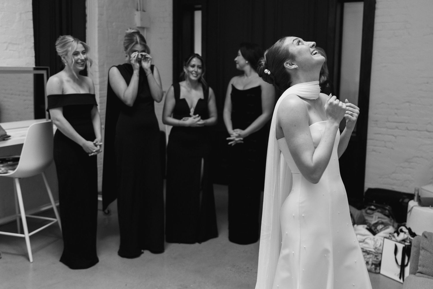 Bridesmaids in black gowns stand together as one person in white takes a drink in elegant preparation.