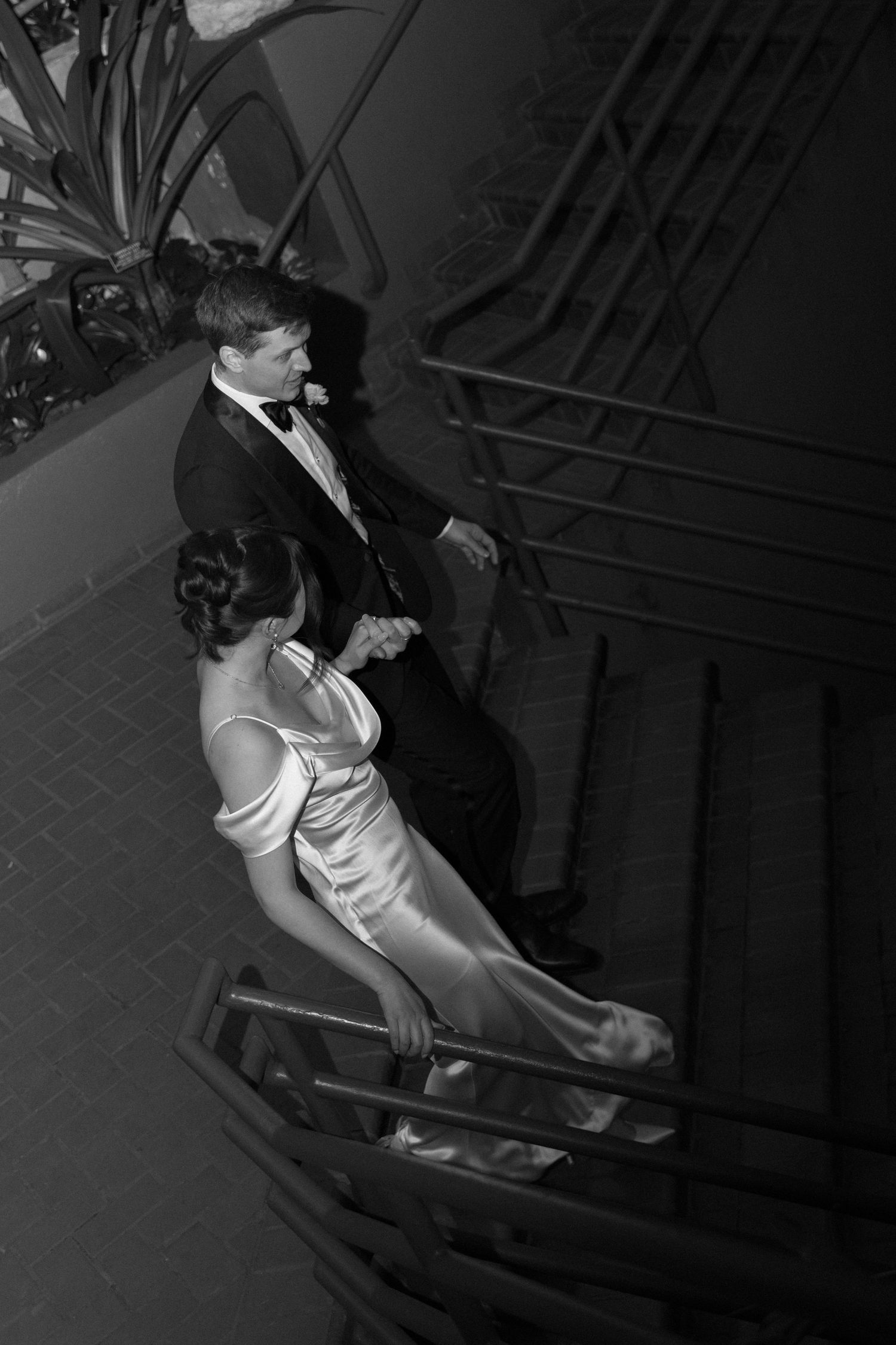 Black and white photos of a couple descending elegant stairs in formal wedding attire.