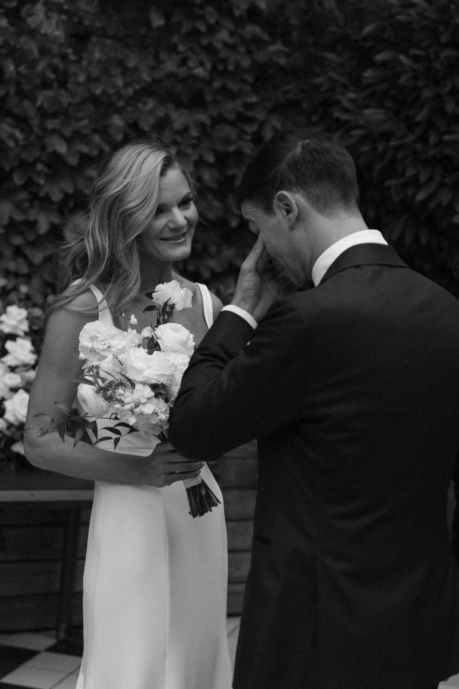 An emotional moment between newlyweds as the bride holds a white floral bouquet.