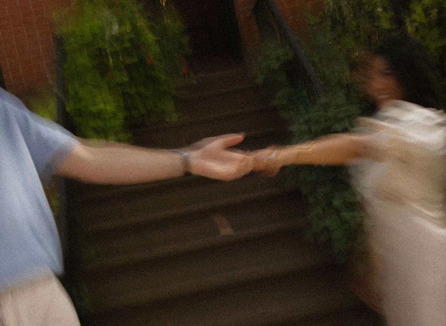 Two hands reaching towards each other in motion on outdoor steps surrounded by greenery.