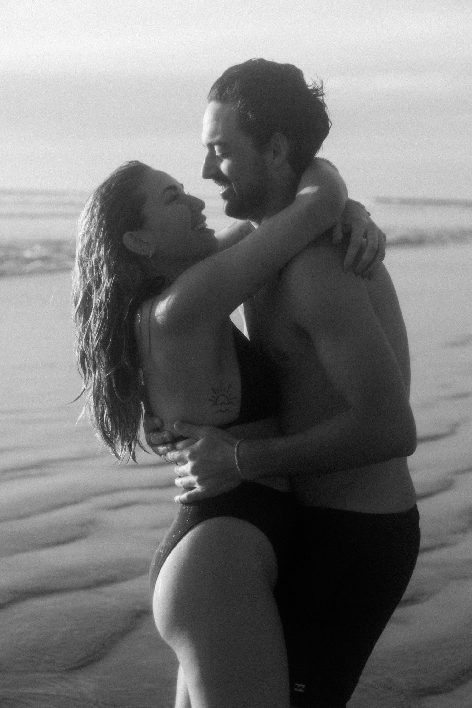 A romantic black and white photo of a couple embracing on the beach at sunset.