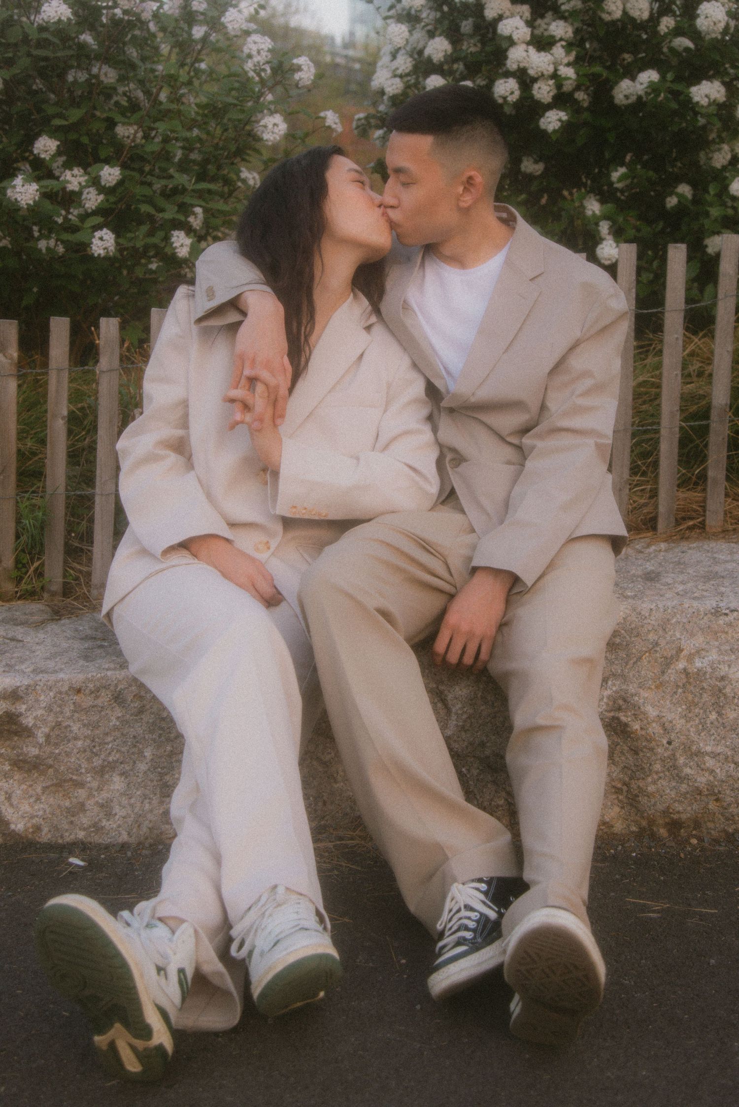Intimate photoshoot of couple in beige attire sitting together by a wooden fence.