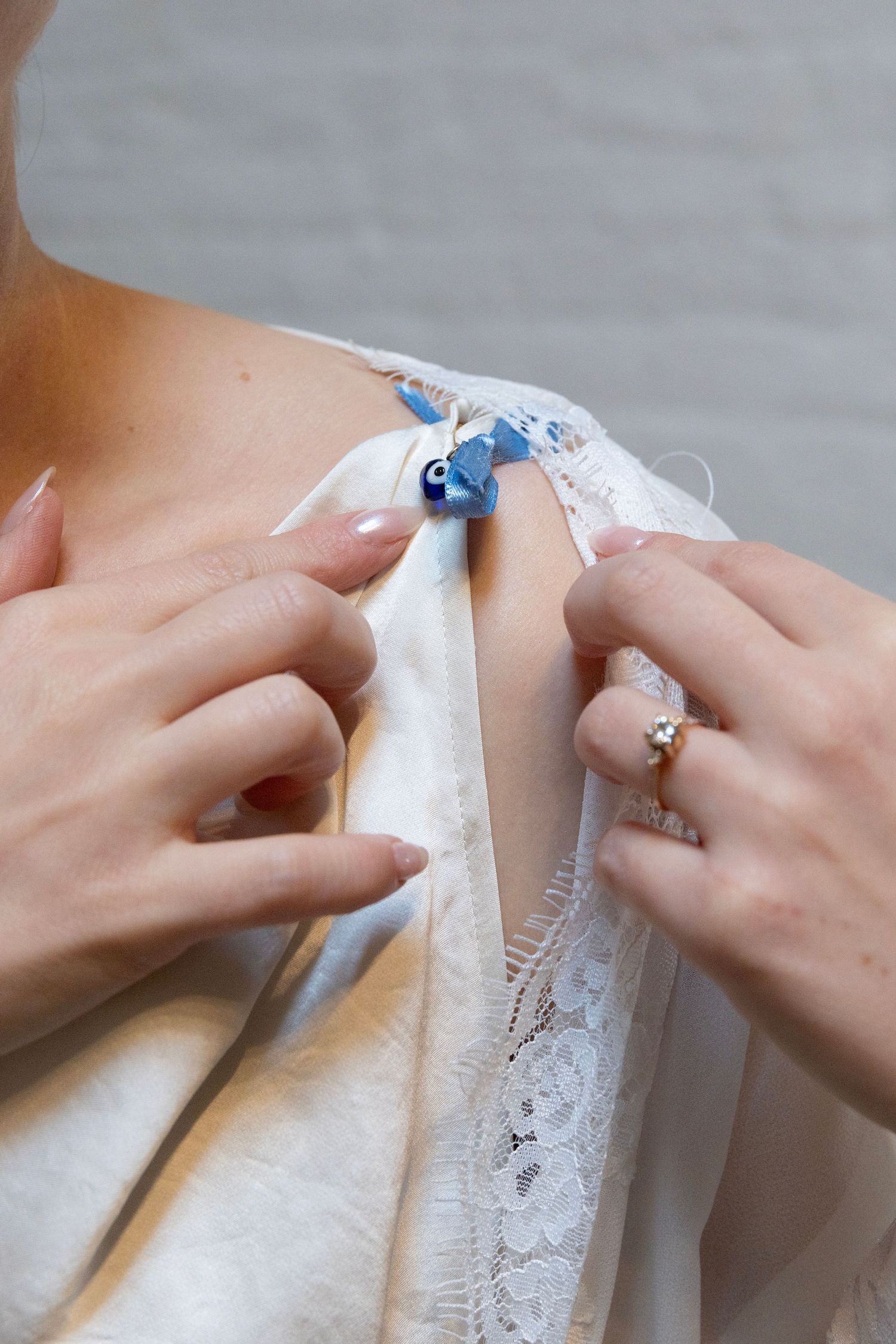 Close-up of hands sewing something blue onto white lace fabric while wearing a delicate engagement ring.