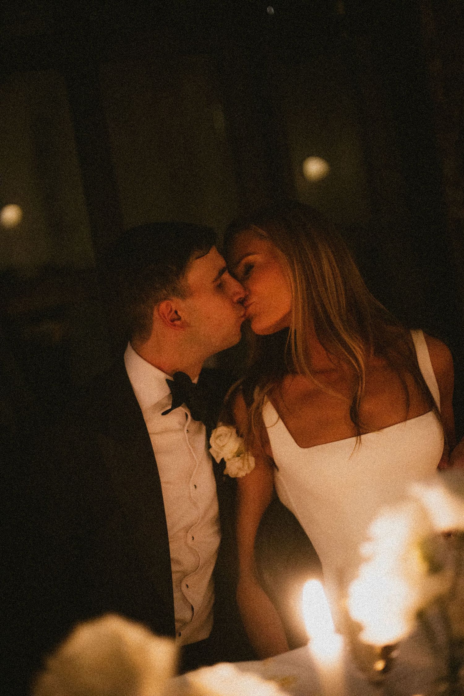 A romantic candlelit moment between a couple sharing a tender kiss in the dark.