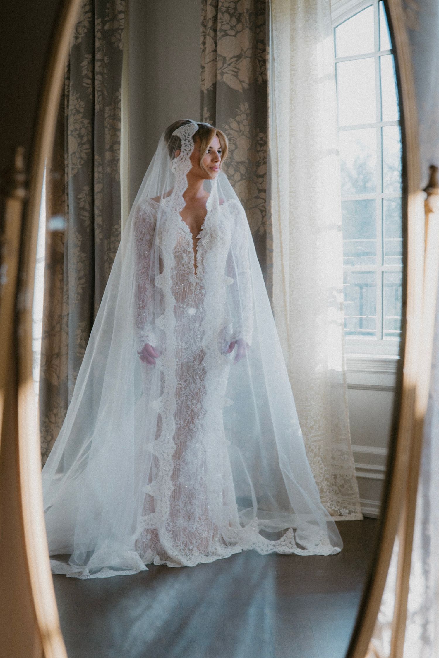 Ethereal reflection of a lace wedding gown and veil in an elegant mirror.