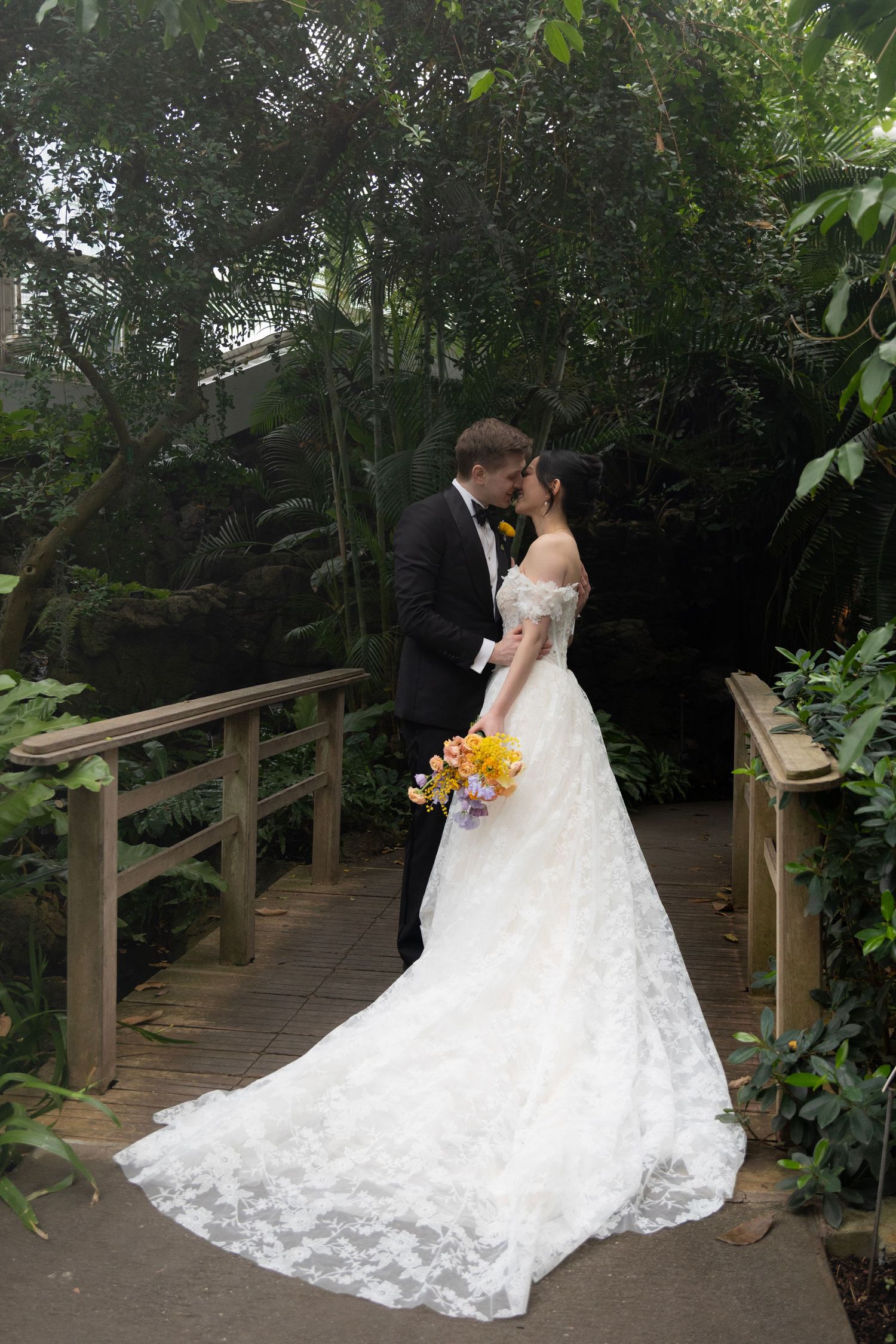 Wedding couple walking along a wooden boardwalk surrounded by lush greenery.