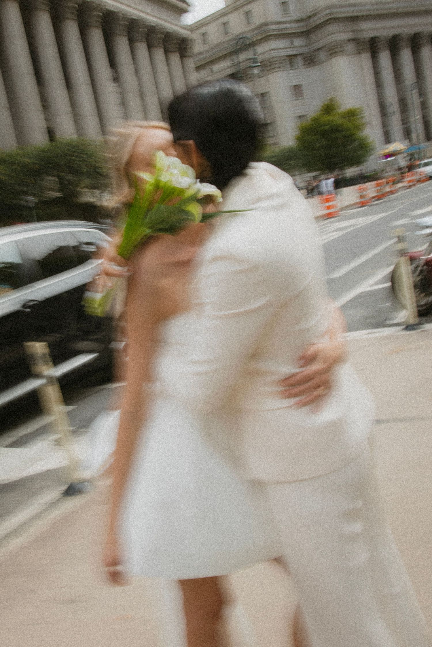 Motion blur captures figures in white attire walking past a grand government building on a city street.