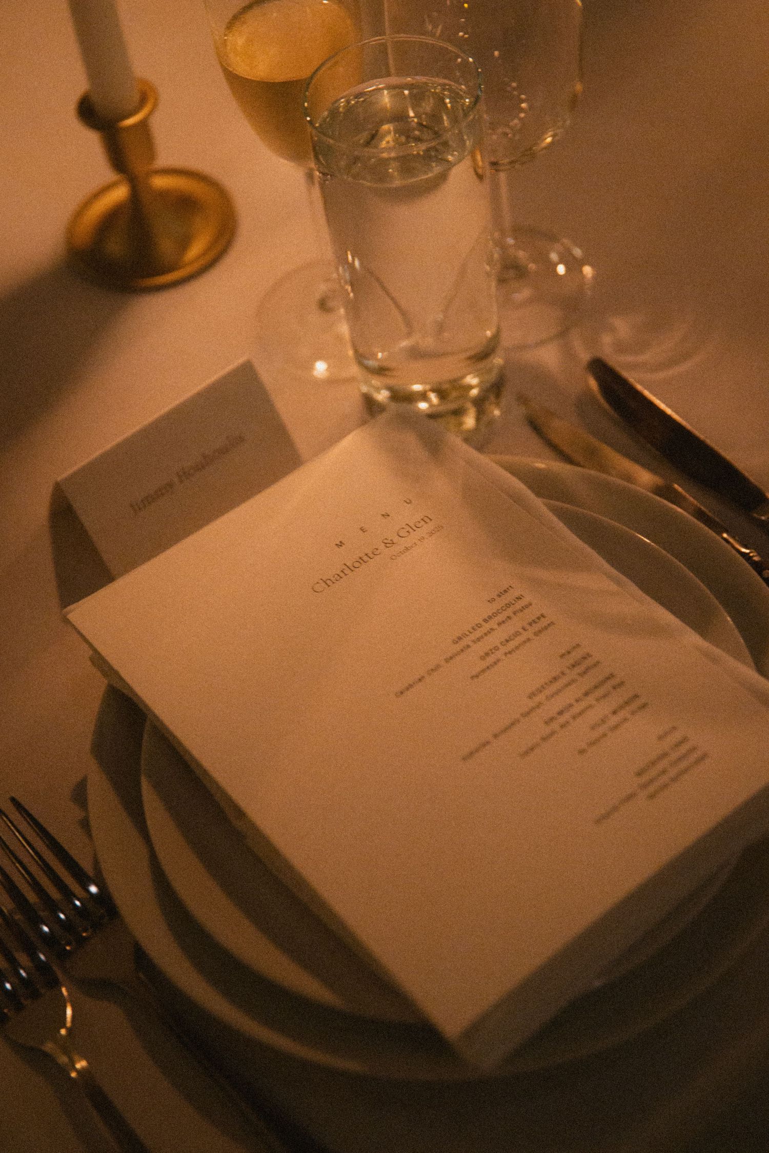 Elegant place settings with menu cards and glassware on a dark table in moody lighting.