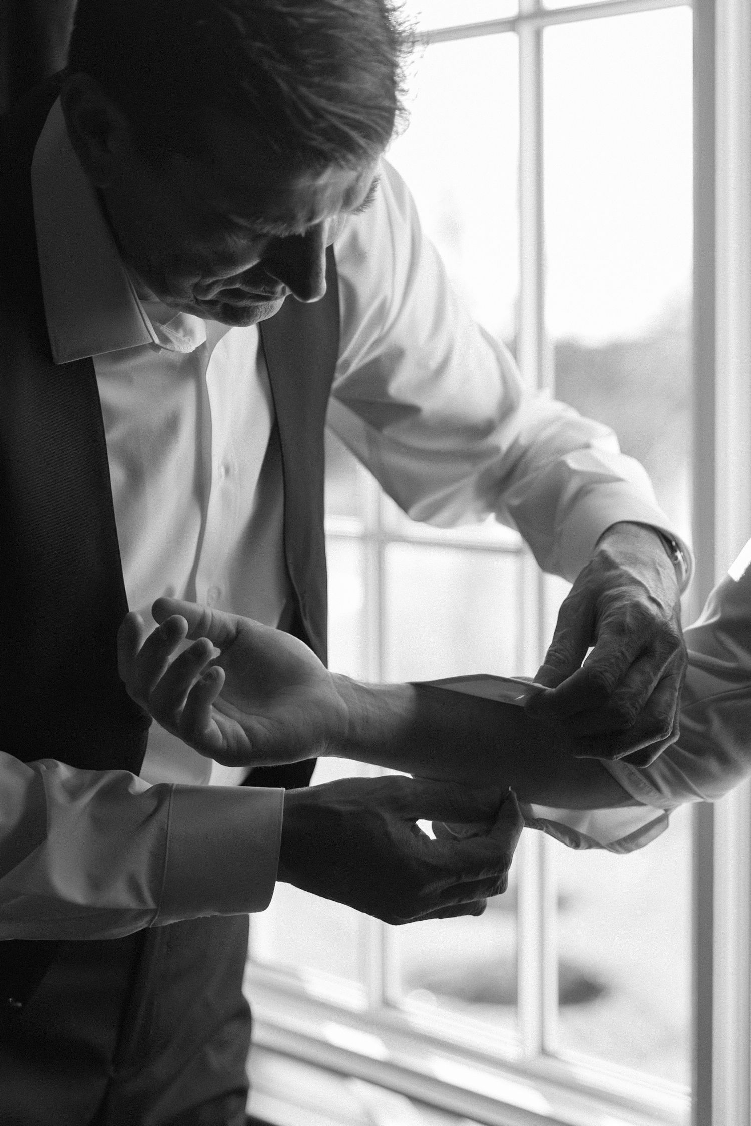 Black and white photo of dress shirt cuff being adjusted near a window.