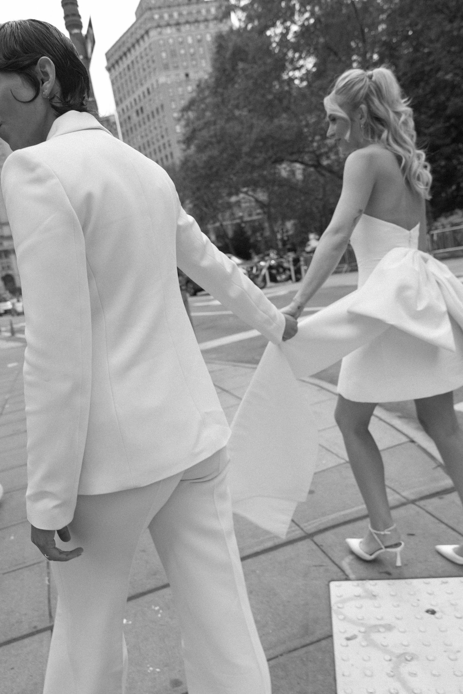 A couple in white outfits dances and poses together in an outdoor urban setting.