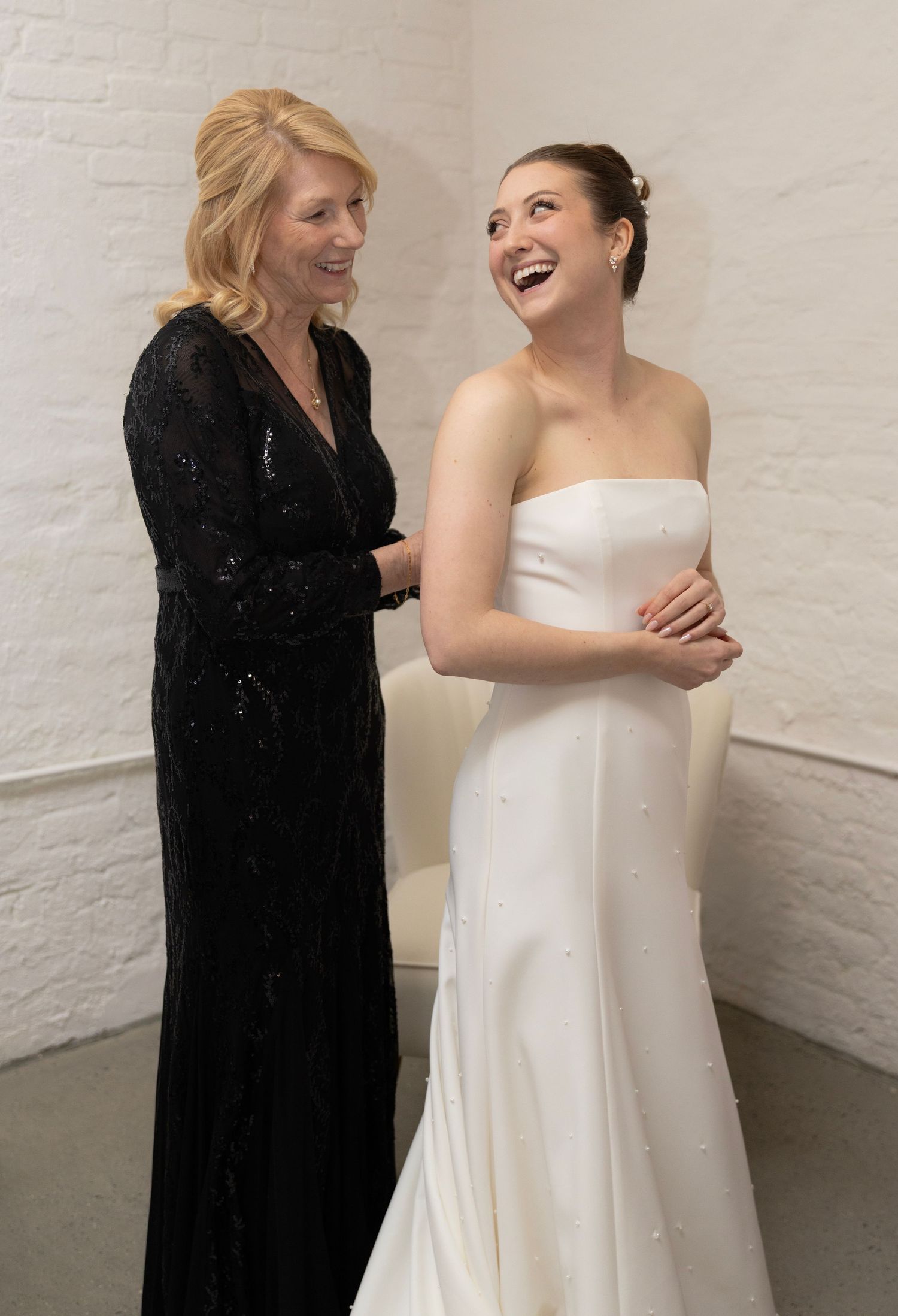 Two people share a joyful moment during a formal event with one wearing a black gown and another in a white wedding dress.