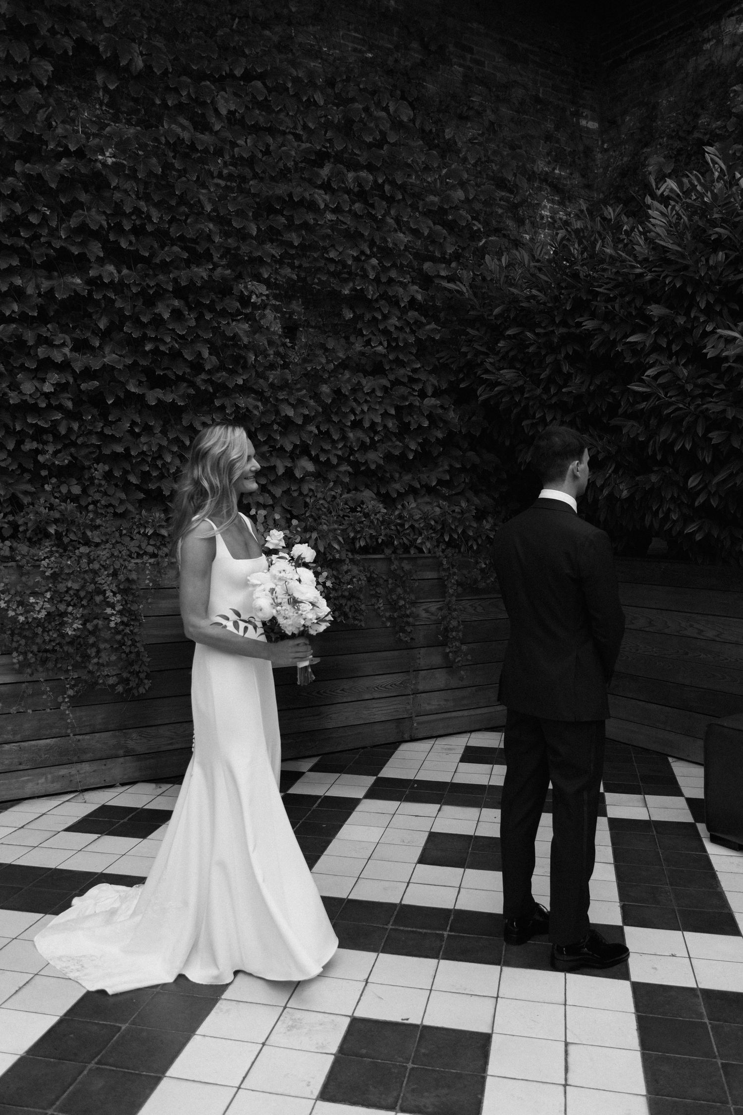 A sequence of black and white wedding photos showing a couple on a checkered tile patio with greenery backdrop.