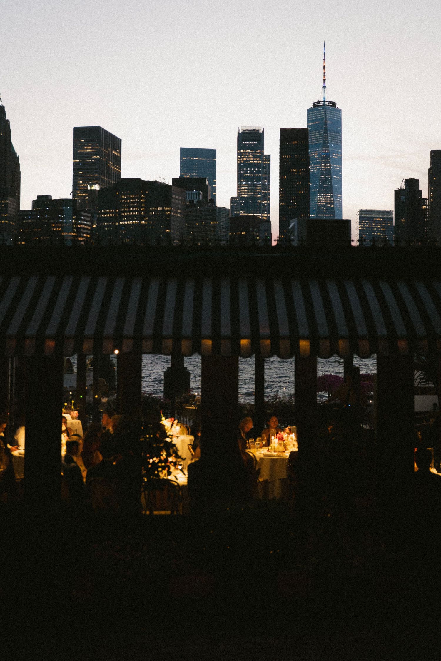 Outdoor dining event at dusk with NYC skyline and One World Trade Center in the background.
