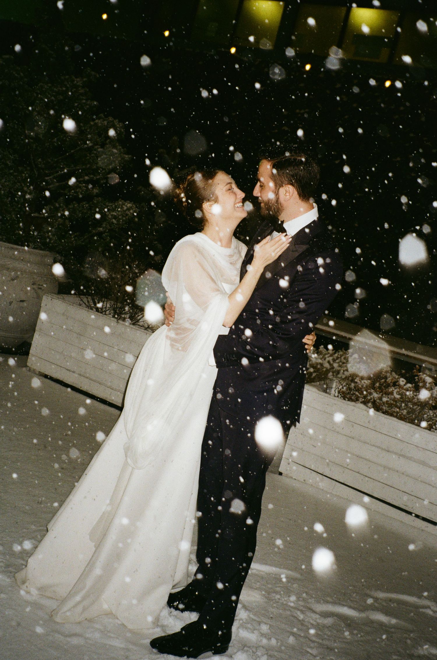 A romantic winter wedding moment captured in the snow with illuminated snowflakes falling around a dancing couple.