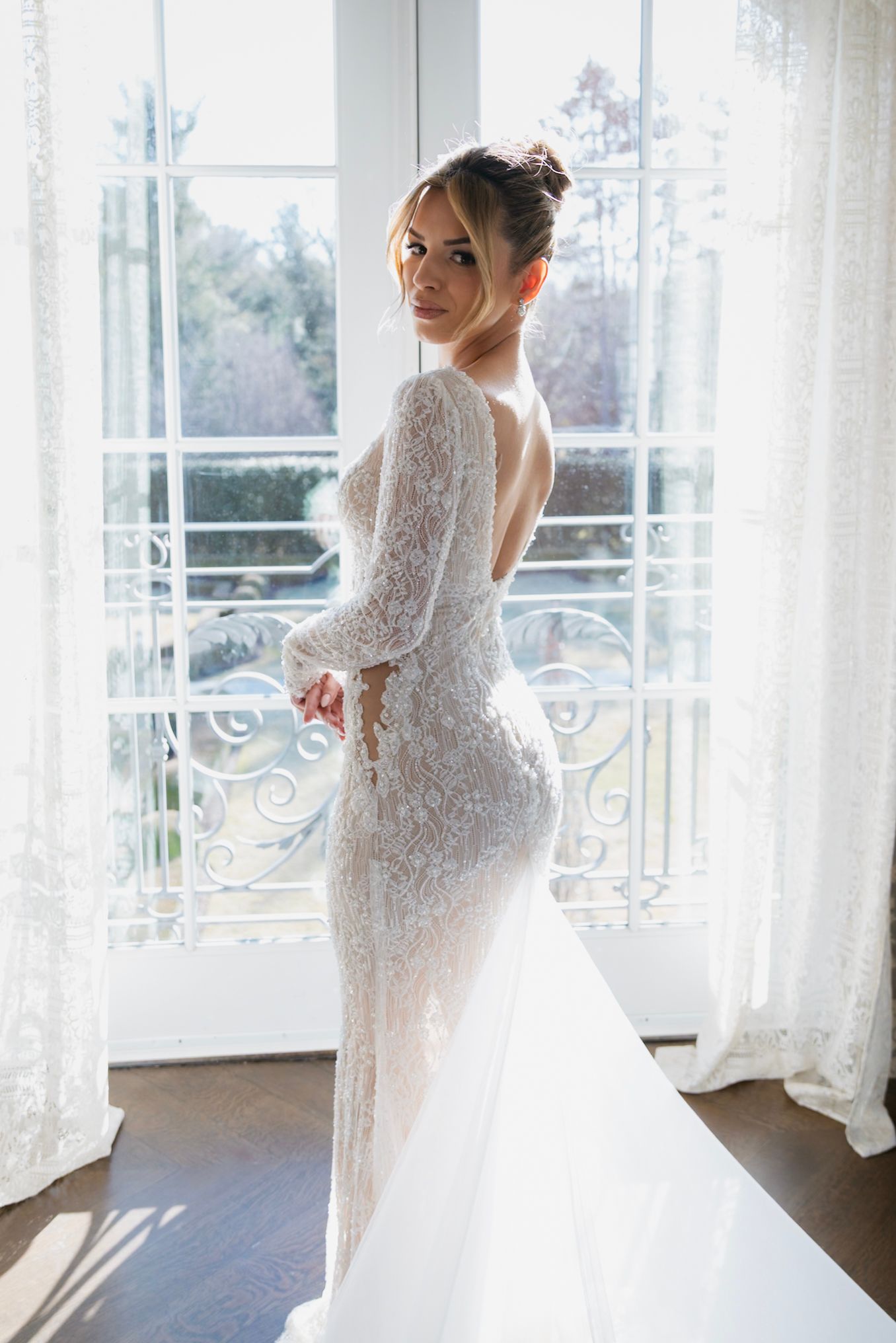 A bride in an elegant lace wedding dress stands near bright windows in multiple romantic posed shots.