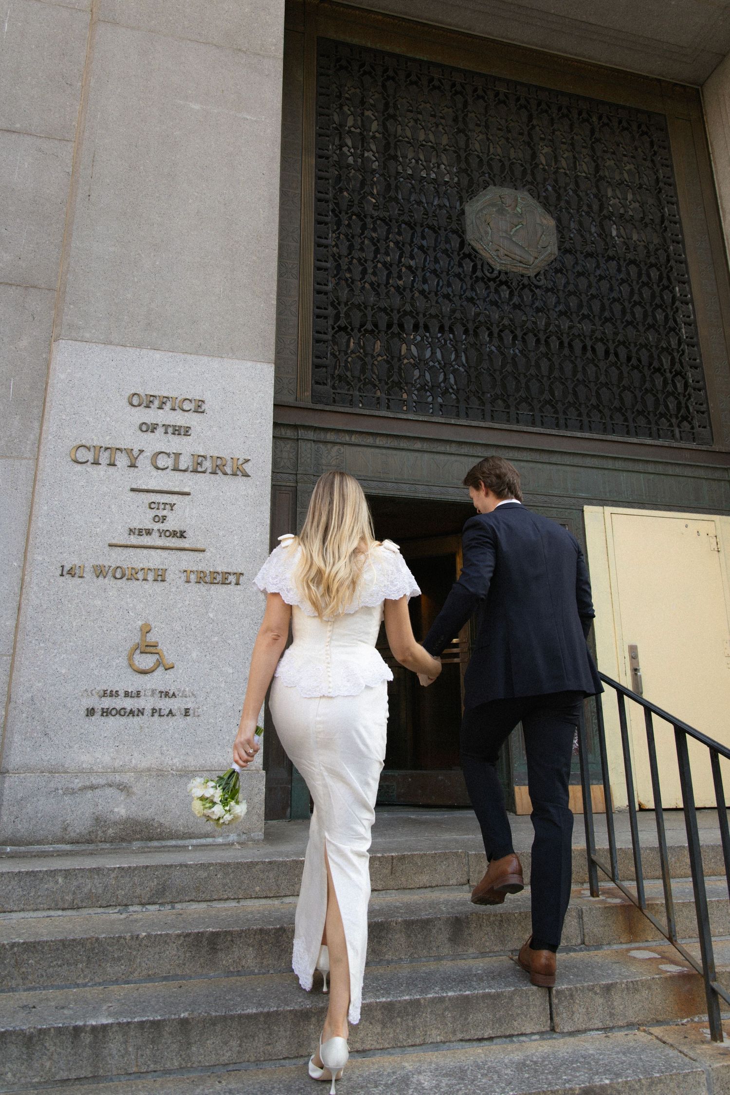 Couple in wedding attire climbing steps to NYC Office of the City Clerk at 141 Worth Street for their civil ceremony.