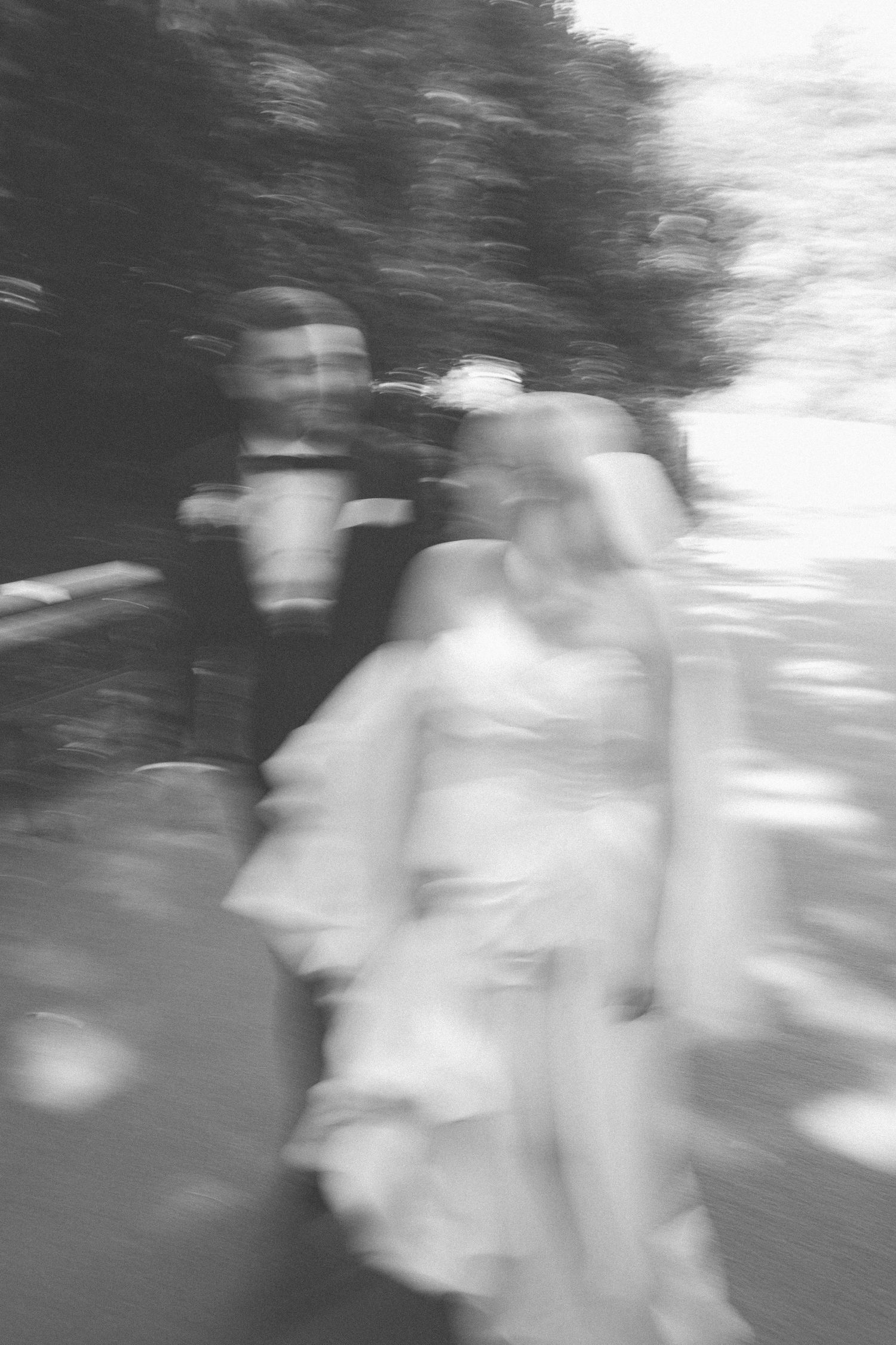 A blurred black and white photograph of a couple in formal attire walking outdoors in a dreamlike motion effect.