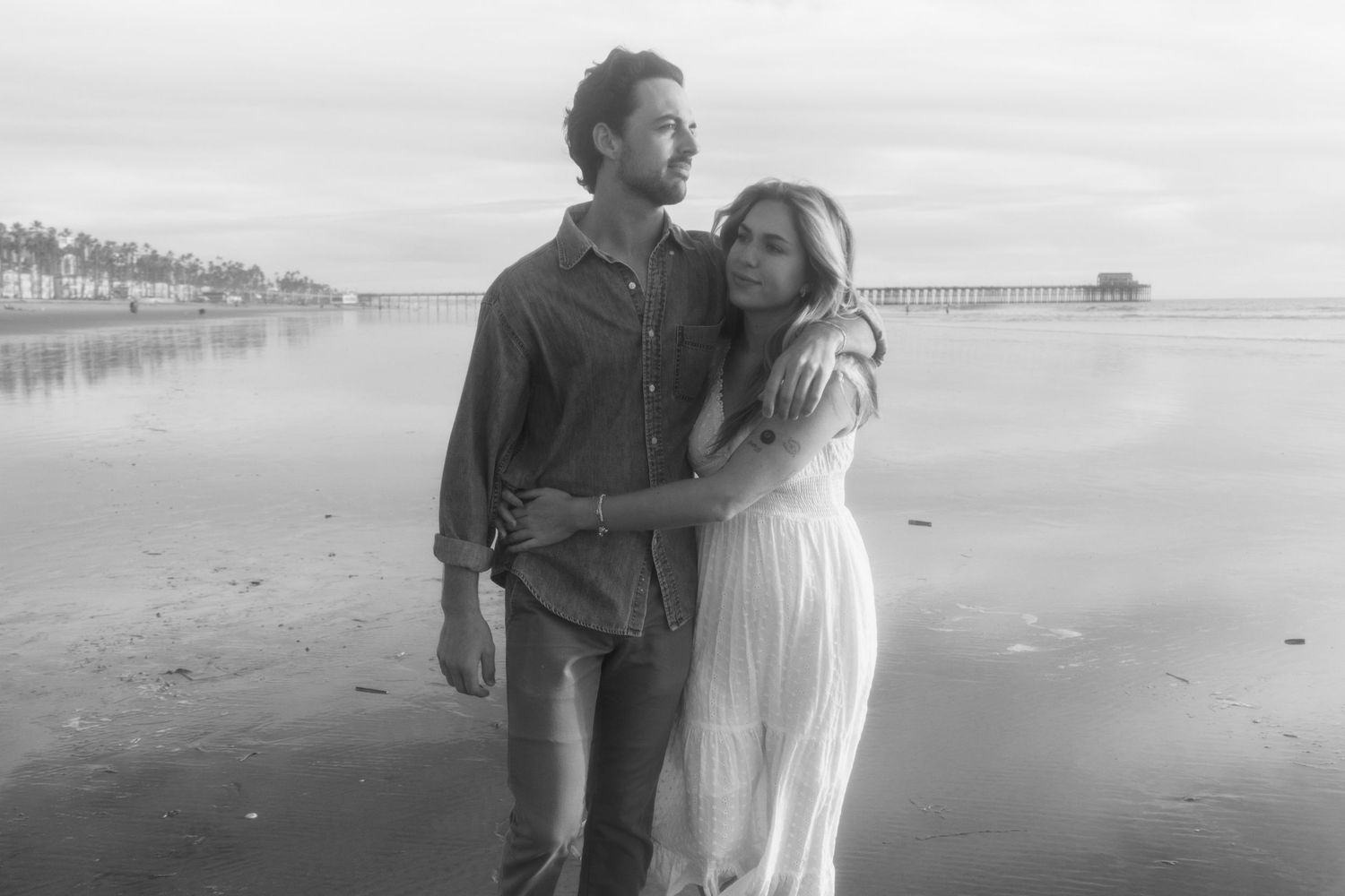 A series of romantic black and white beach photos showing a couple embracing on a sandy shoreline at sunset.