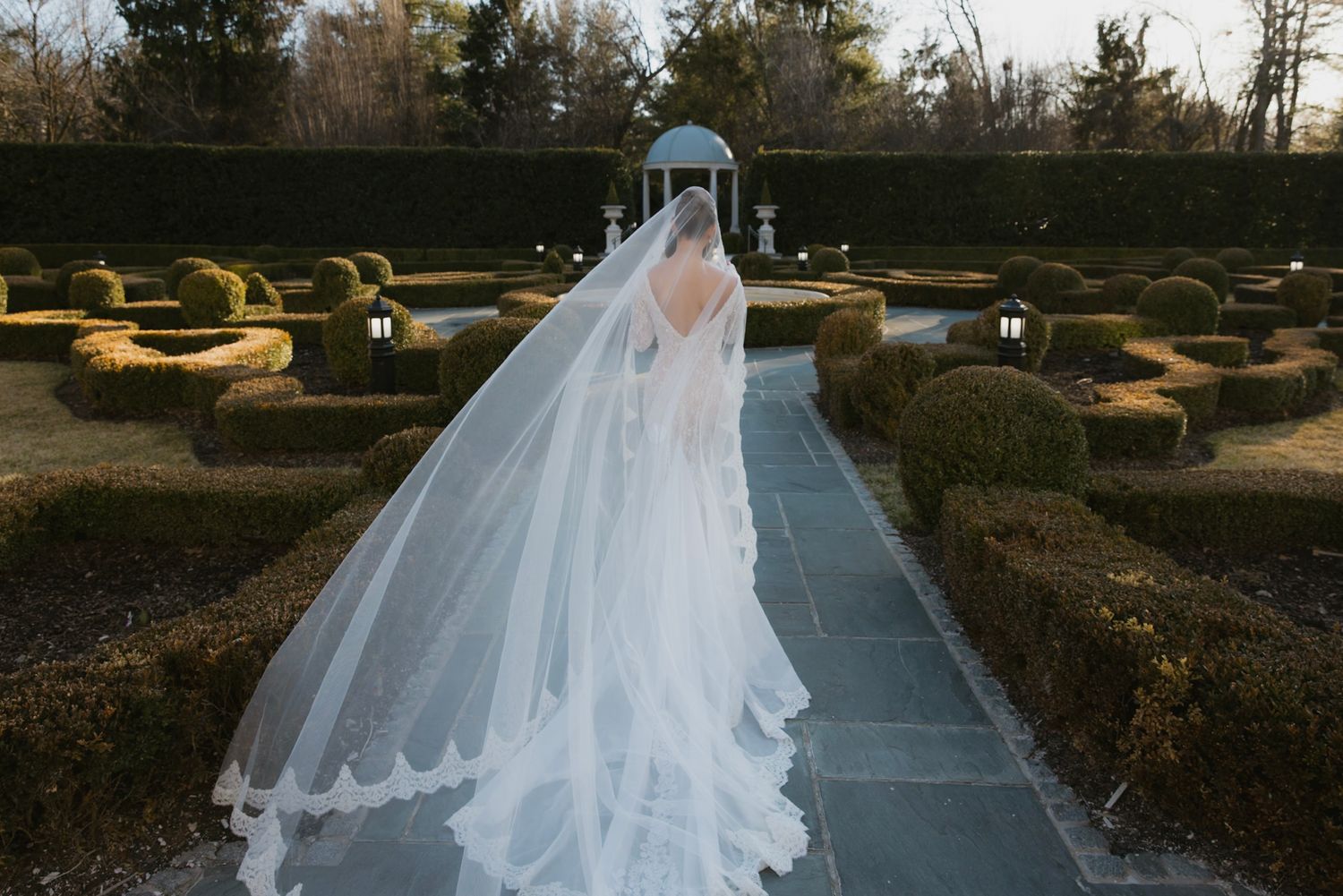 Long flowing wedding dress trail photographed in an outdoor garden setting.