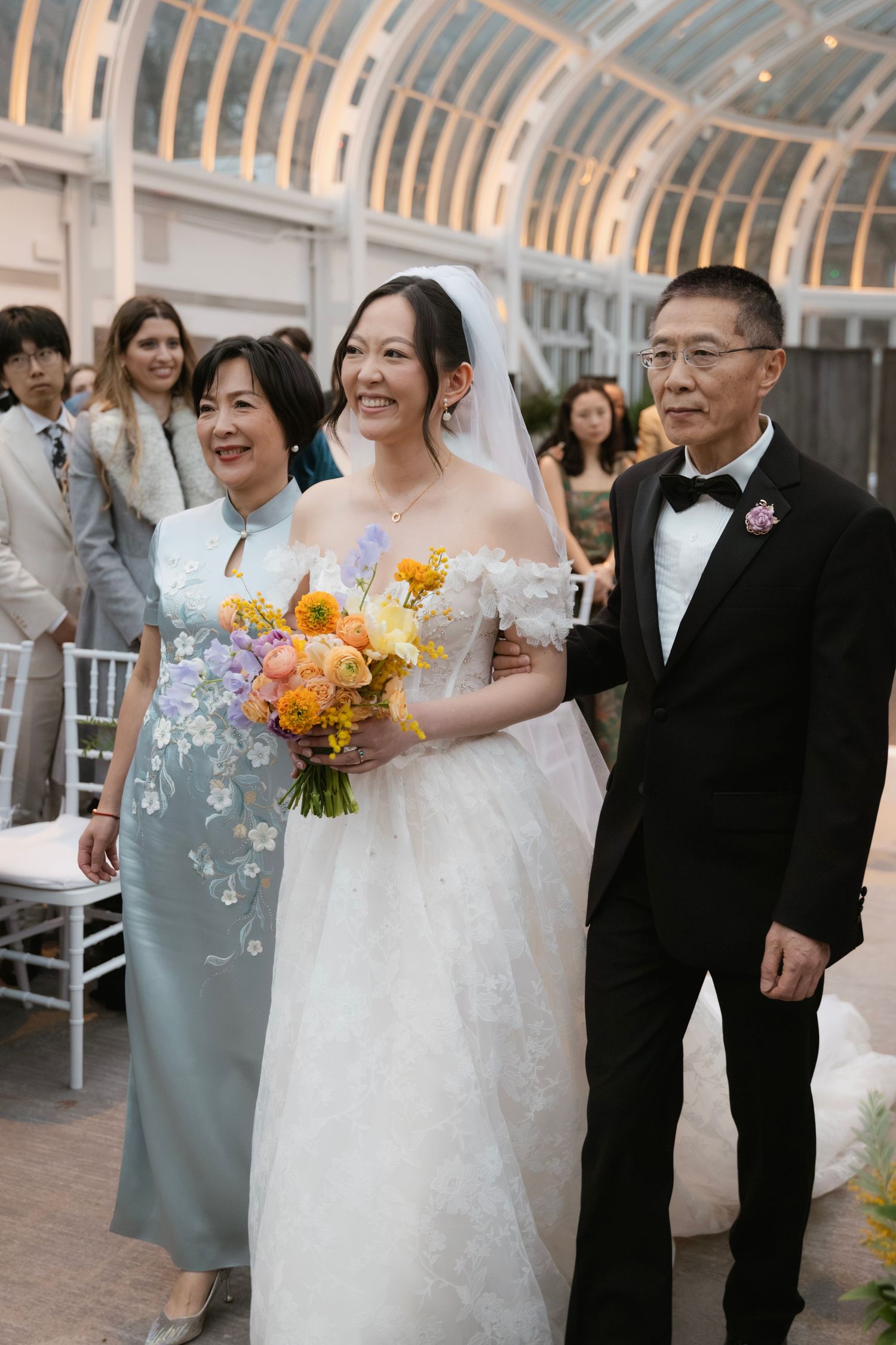 Traditional wedding ceremony in glass-domed venue with vibrant orange bouquet.