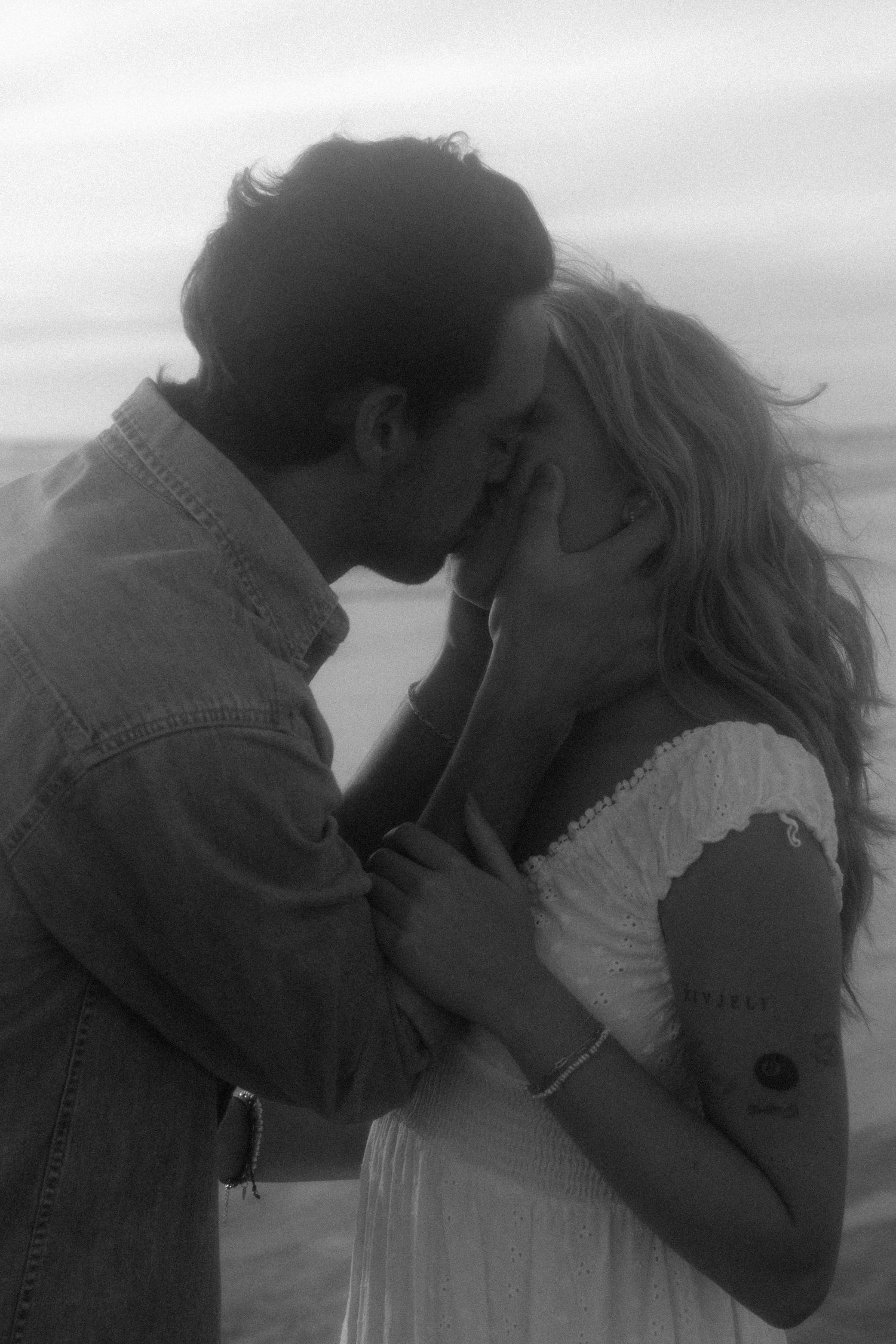 A romantic black and white photo sequence showing a couple in an intimate embrace and kiss against a cloudy sky backdrop.