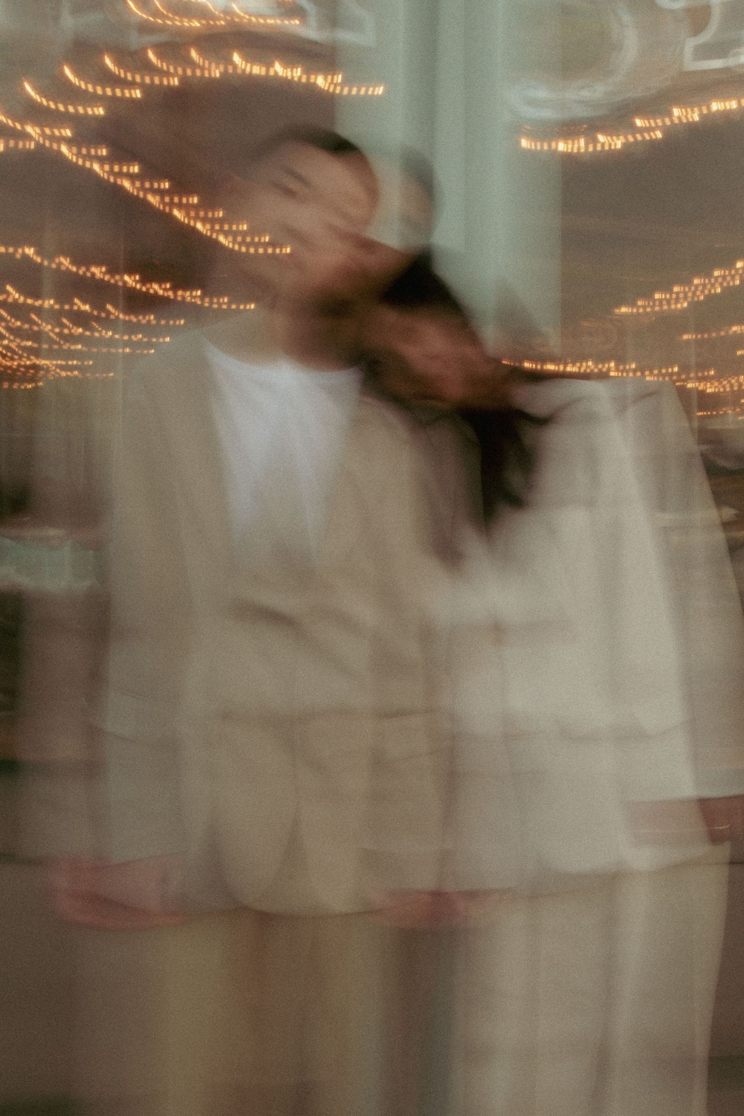 Blurred motion photograph showing a figure in white clothing with glowing string lights creating ethereal trails in the background.