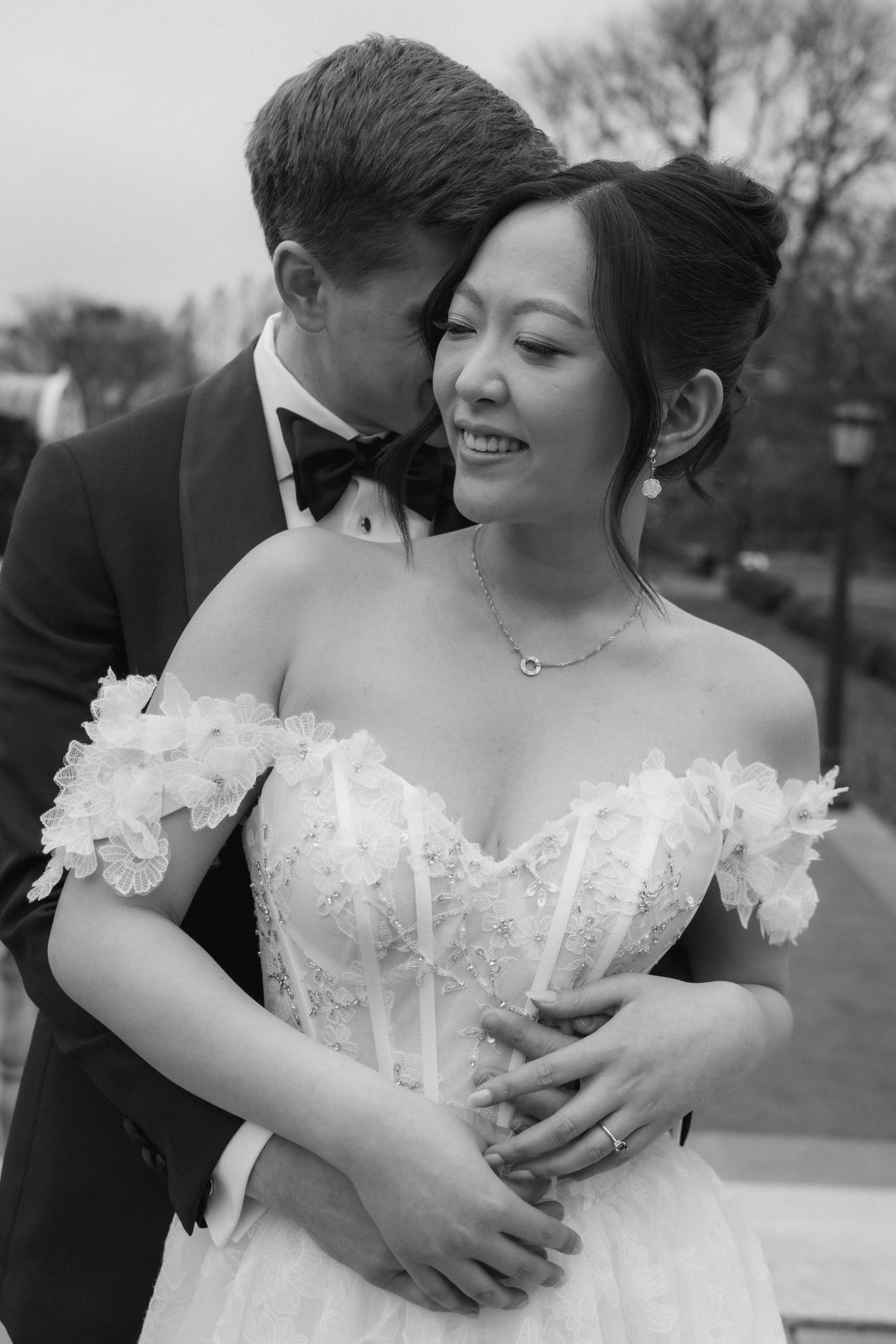A romantic black and white wedding portrait showing a couple embracing, with the bride wearing an elegant white off-shoulder gown.