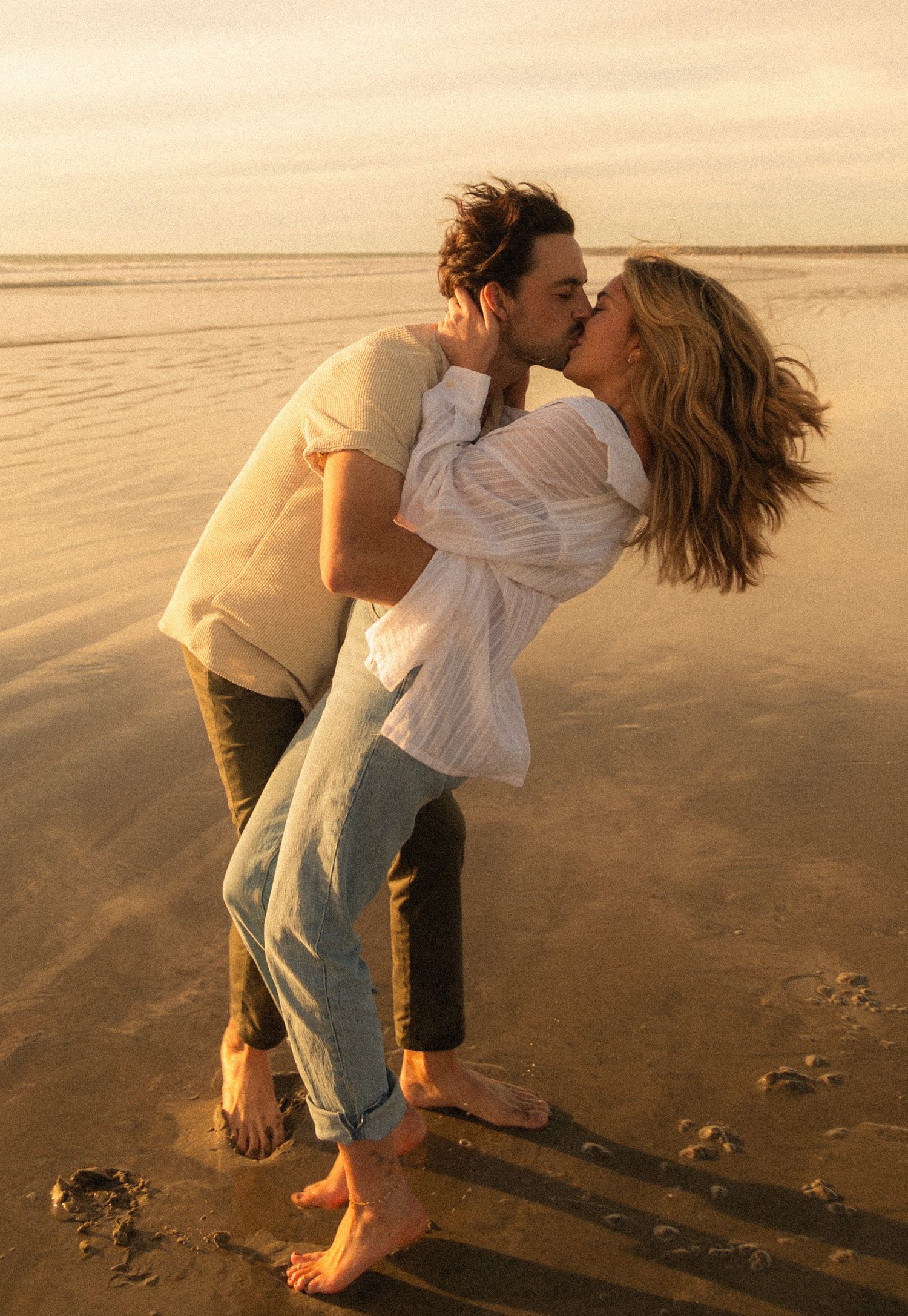 A romantic couple dancing on a sandy beach at sunset creating a playful and carefree moment together.