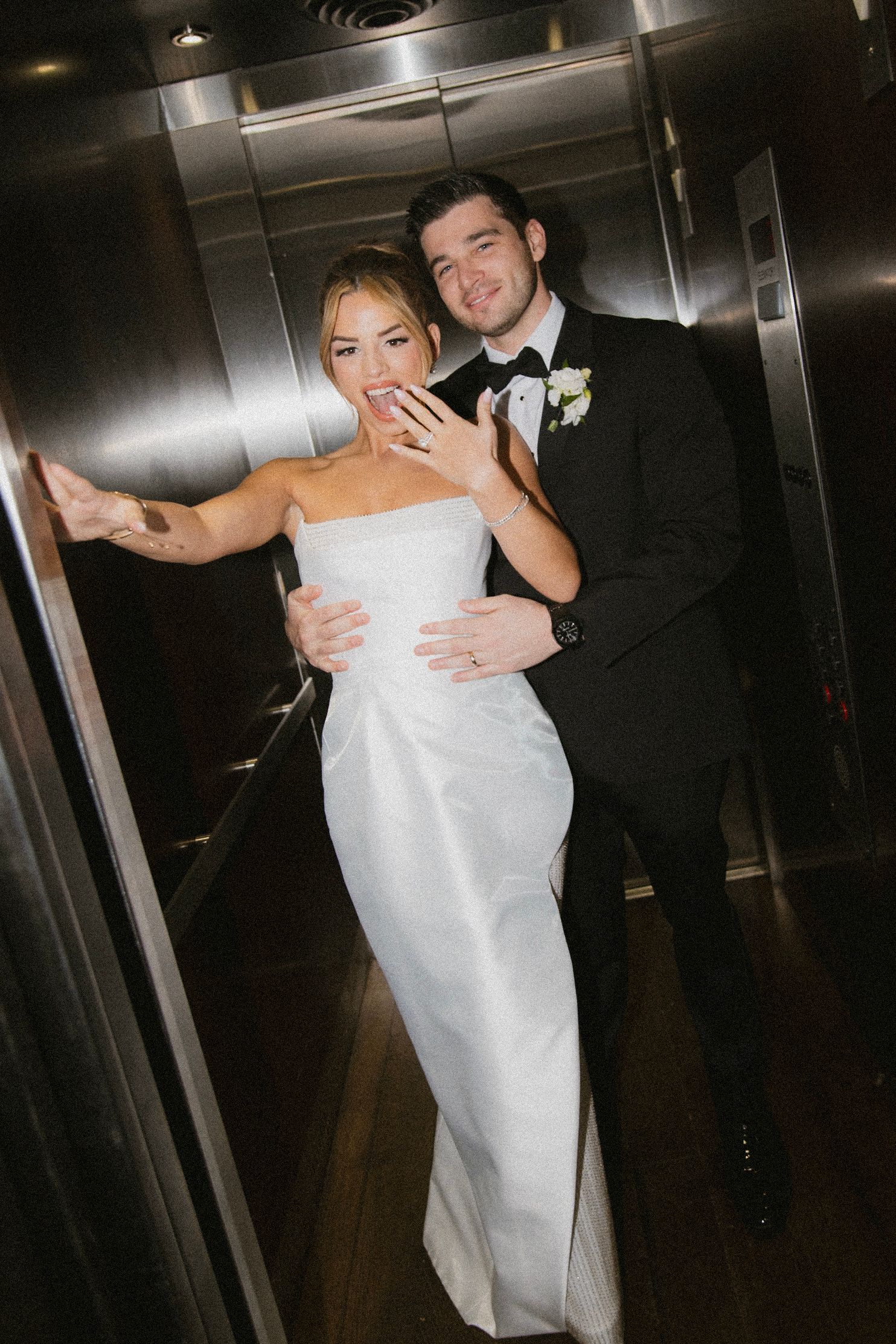 Wedding couple posing together in elevator wearing formal white dress and black tuxedo.