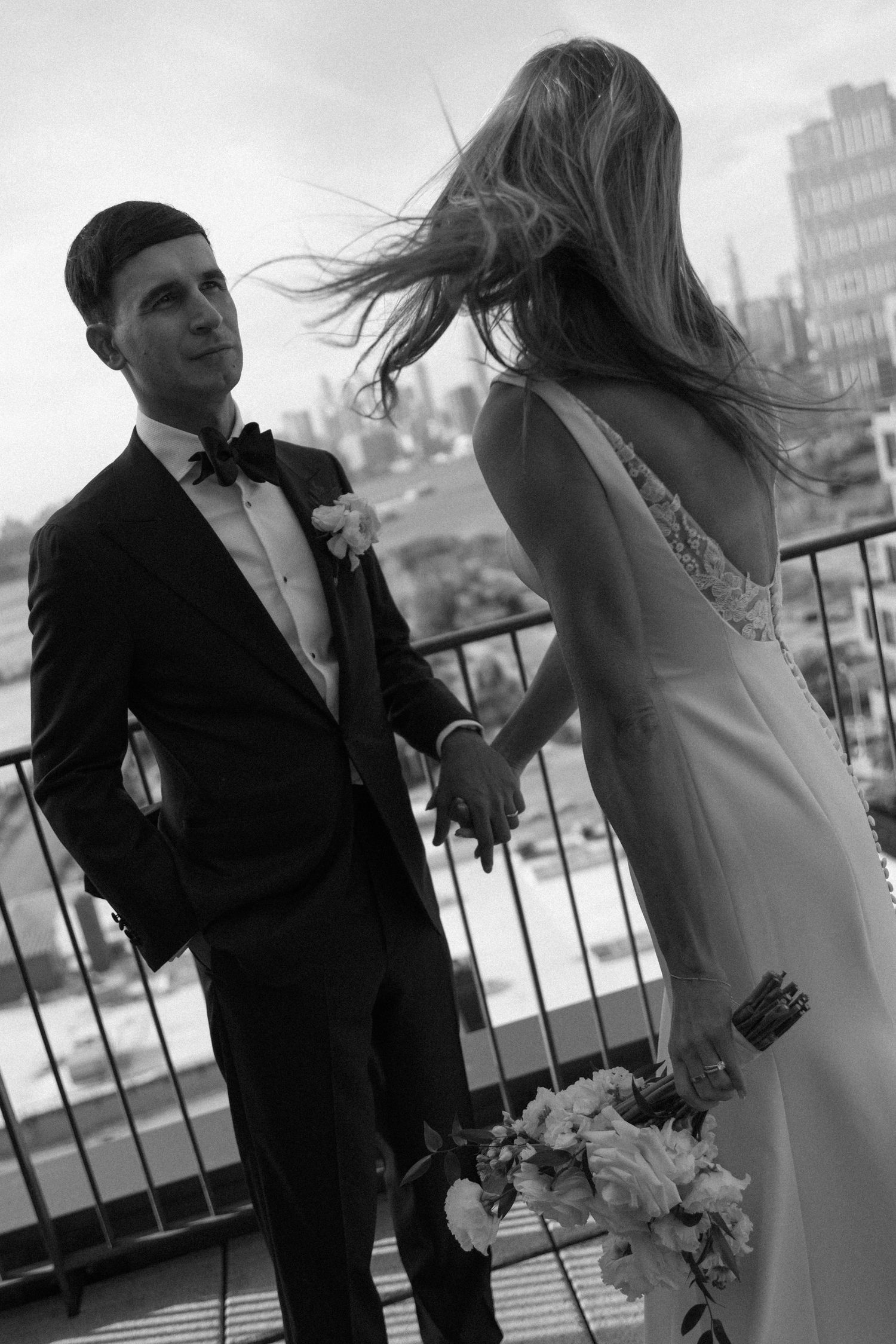 Black and white wedding photo series showing a romantic moment between newlyweds on a city rooftop terrace.