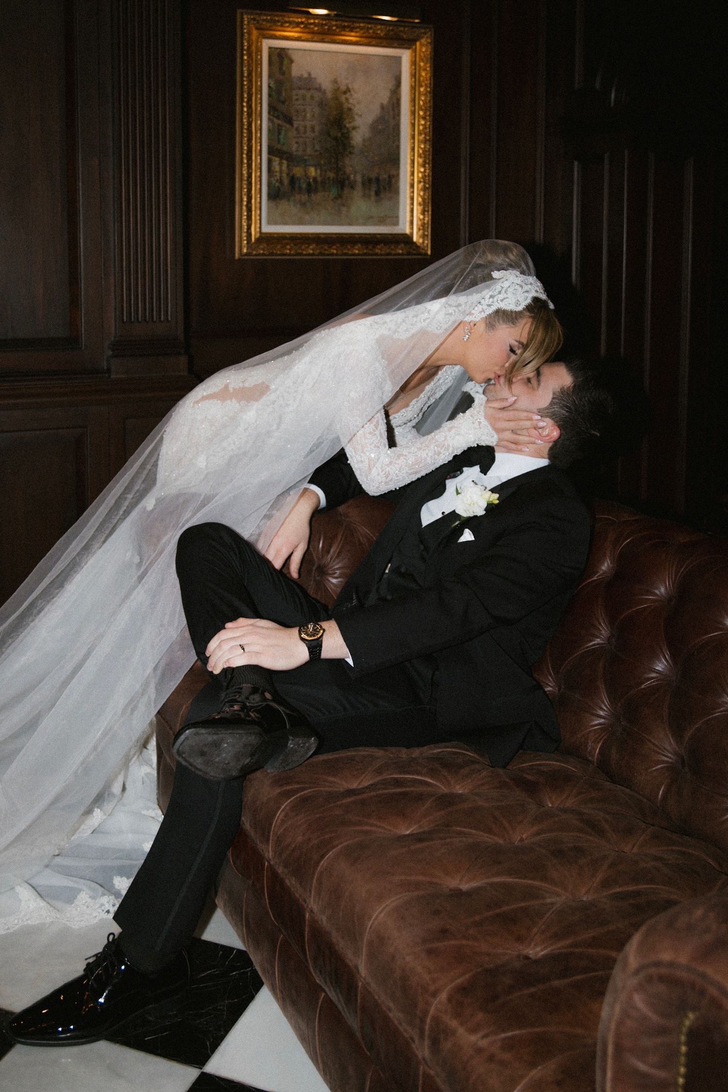 Wedding dress details on brown leather couch in dramatic lighting showing flowing veil and fabric textures.