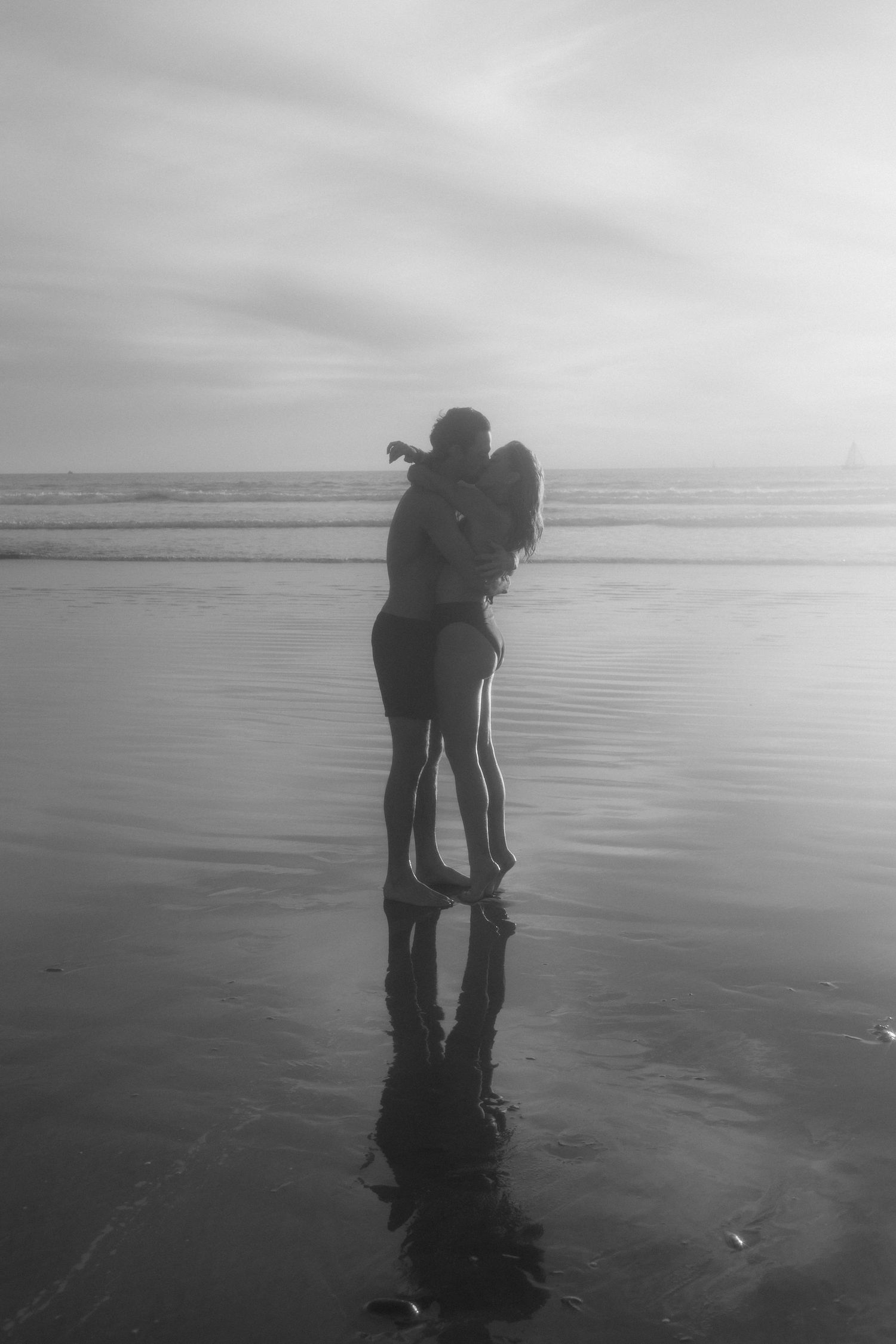A romantic silhouette of a couple embracing on a misty beach at sunset with their reflection in the wet sand.