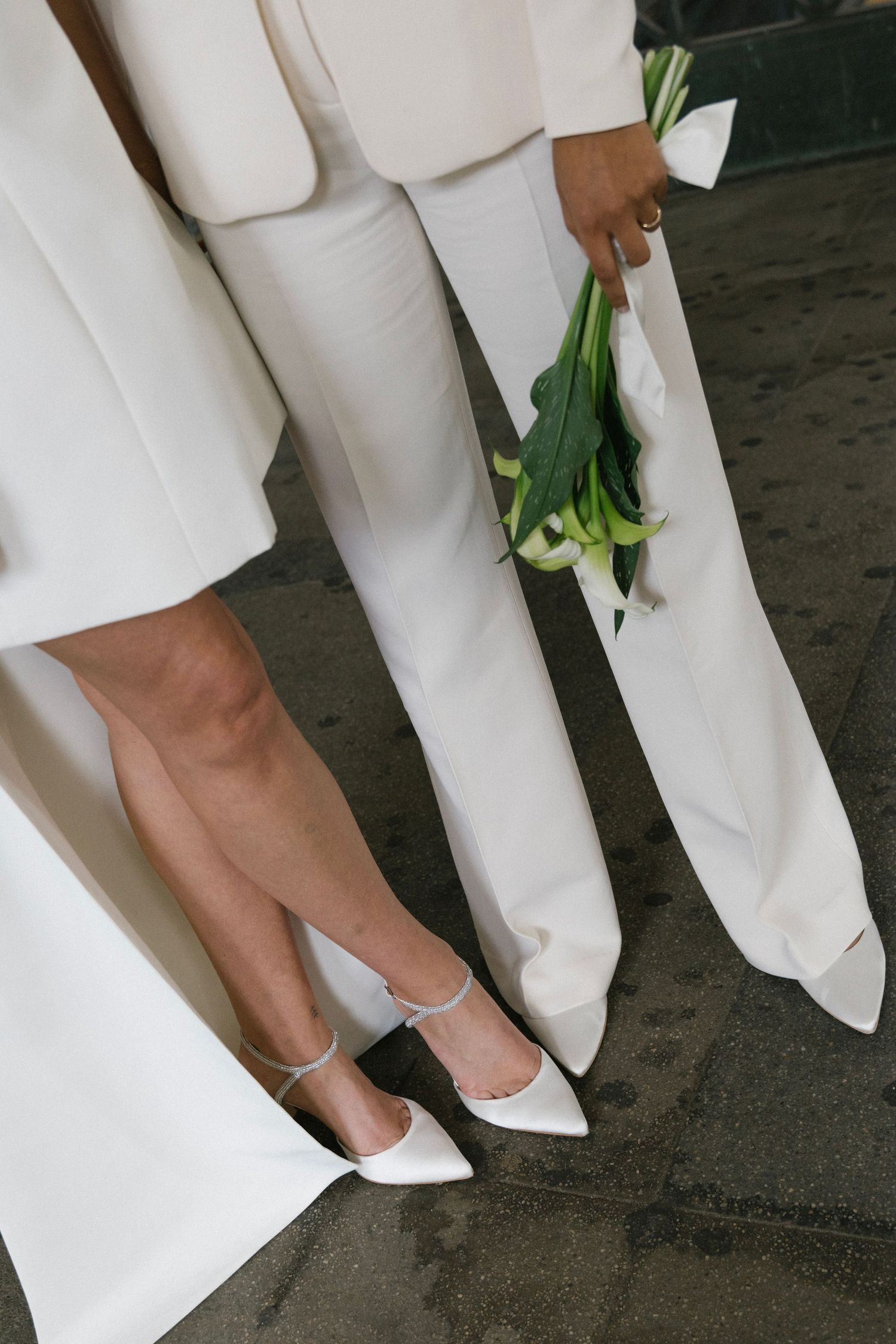 Close-up of two people wearing white pants and matching white shoes while holding fresh tulips.