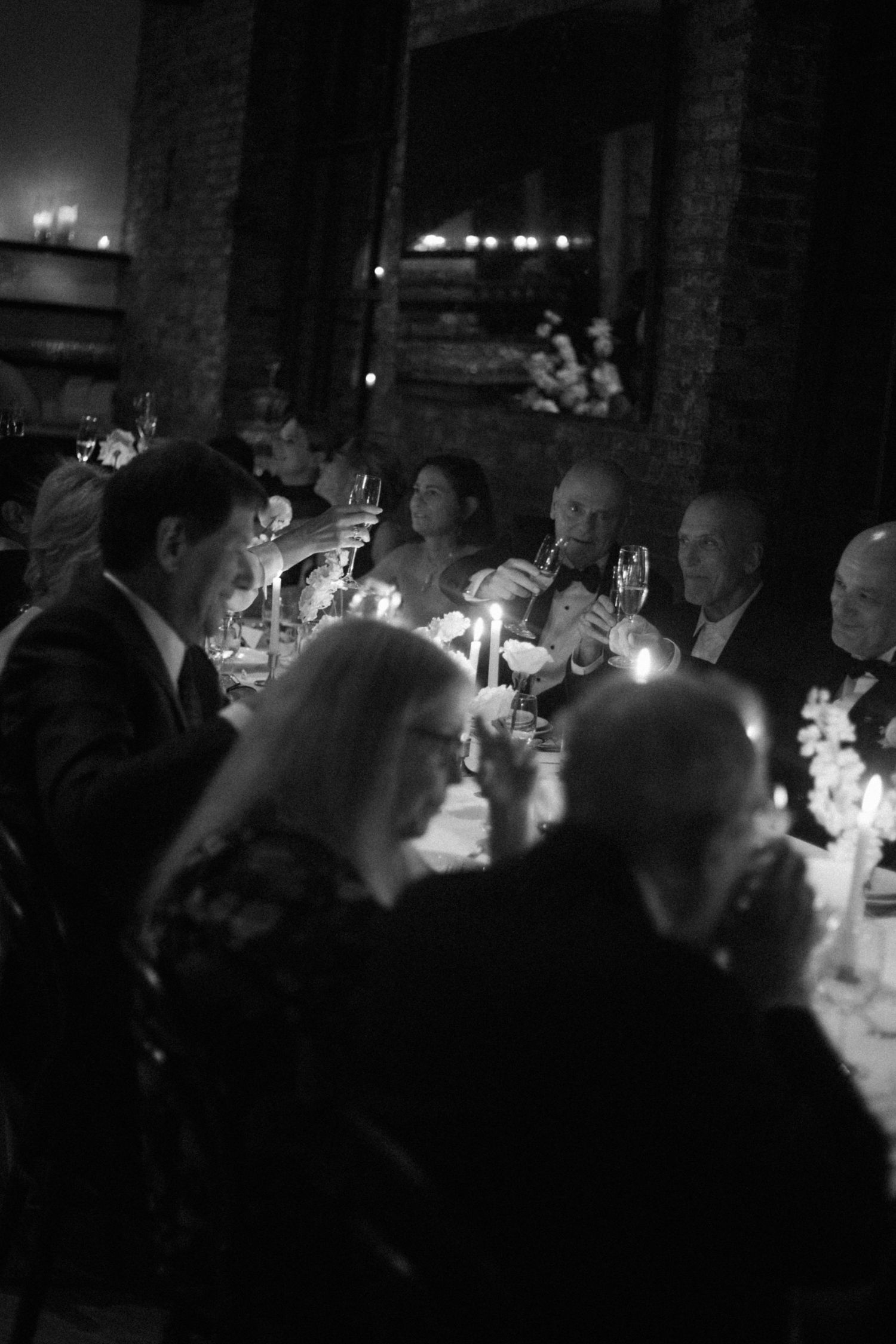 Candlelit dinner event in a dark venue with guests seated at tables illuminated by warm glowing candlelight.